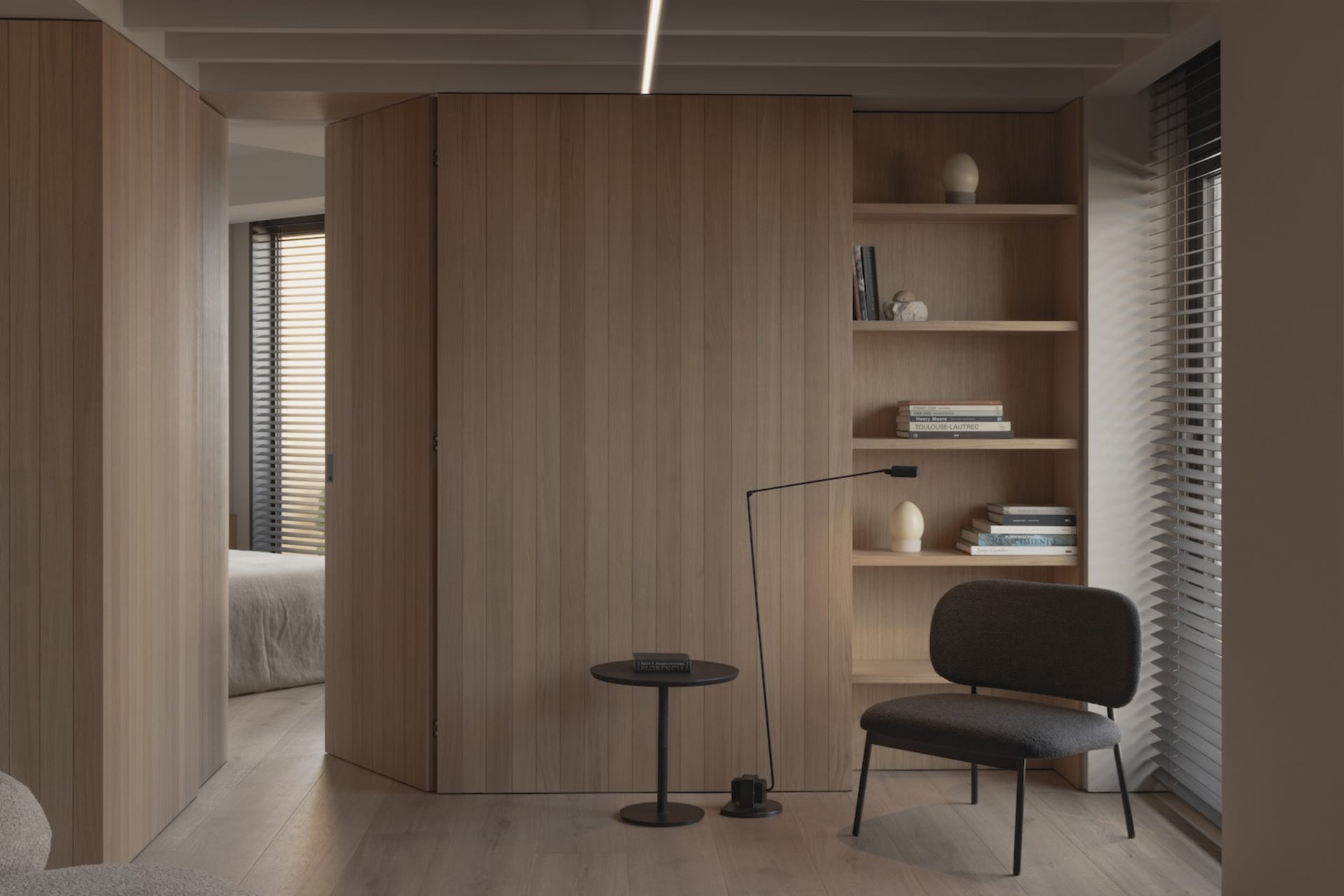 A modern minimalist living room with wood-paneled walls, a black armchair, and a small round table with a lamp.