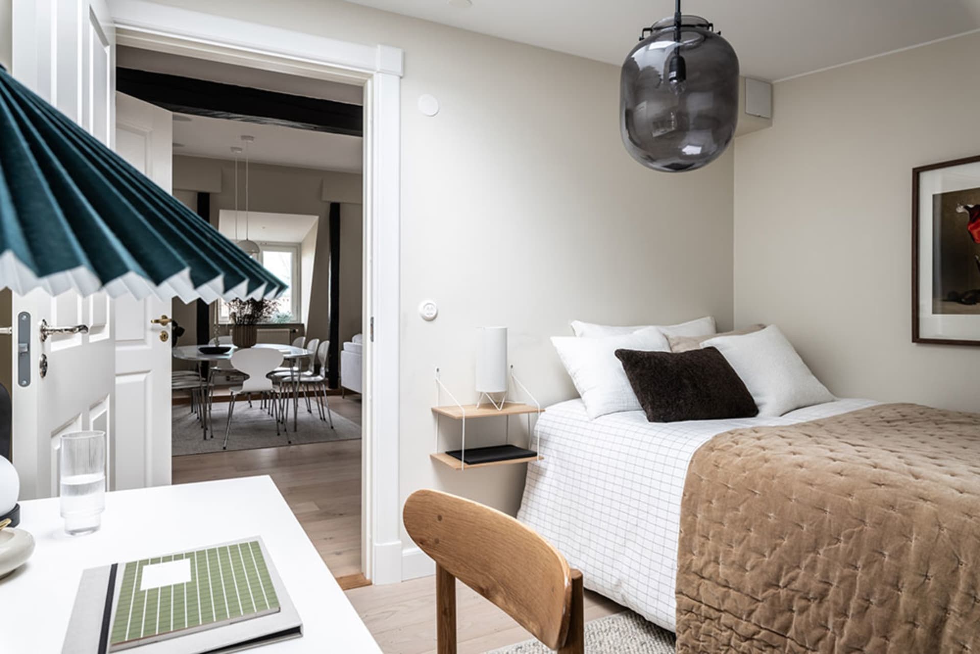 A minimalist bedroom with a bed featuring a textured brown blanket and white sheets, alongside a wooden chair and a green not