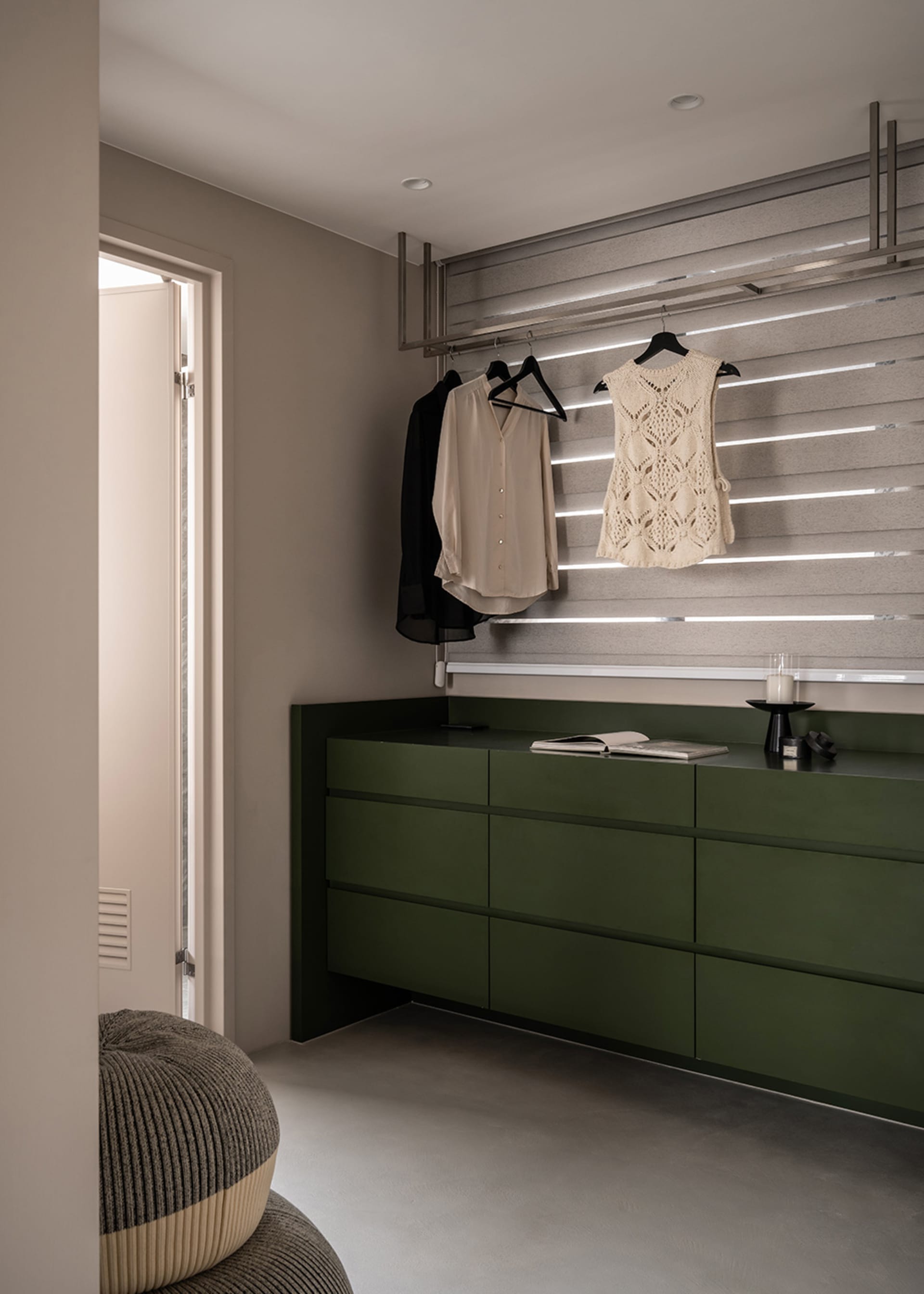 Modern minimalist clothes closet featuring metallic accents, green drawers, and clothes hanging on black hangers.