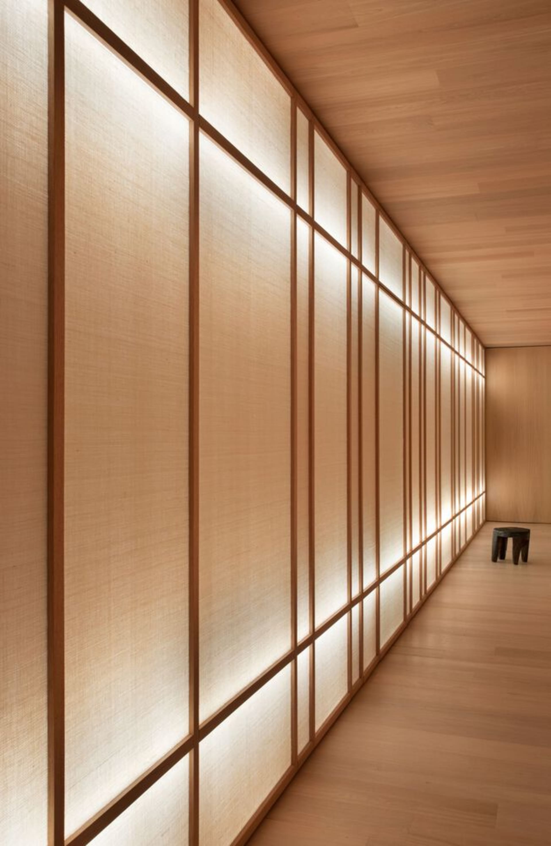 A corridor with wooden walls adorned with rectangular wooden panels filled with warm, ambient lighting, creating a serene and