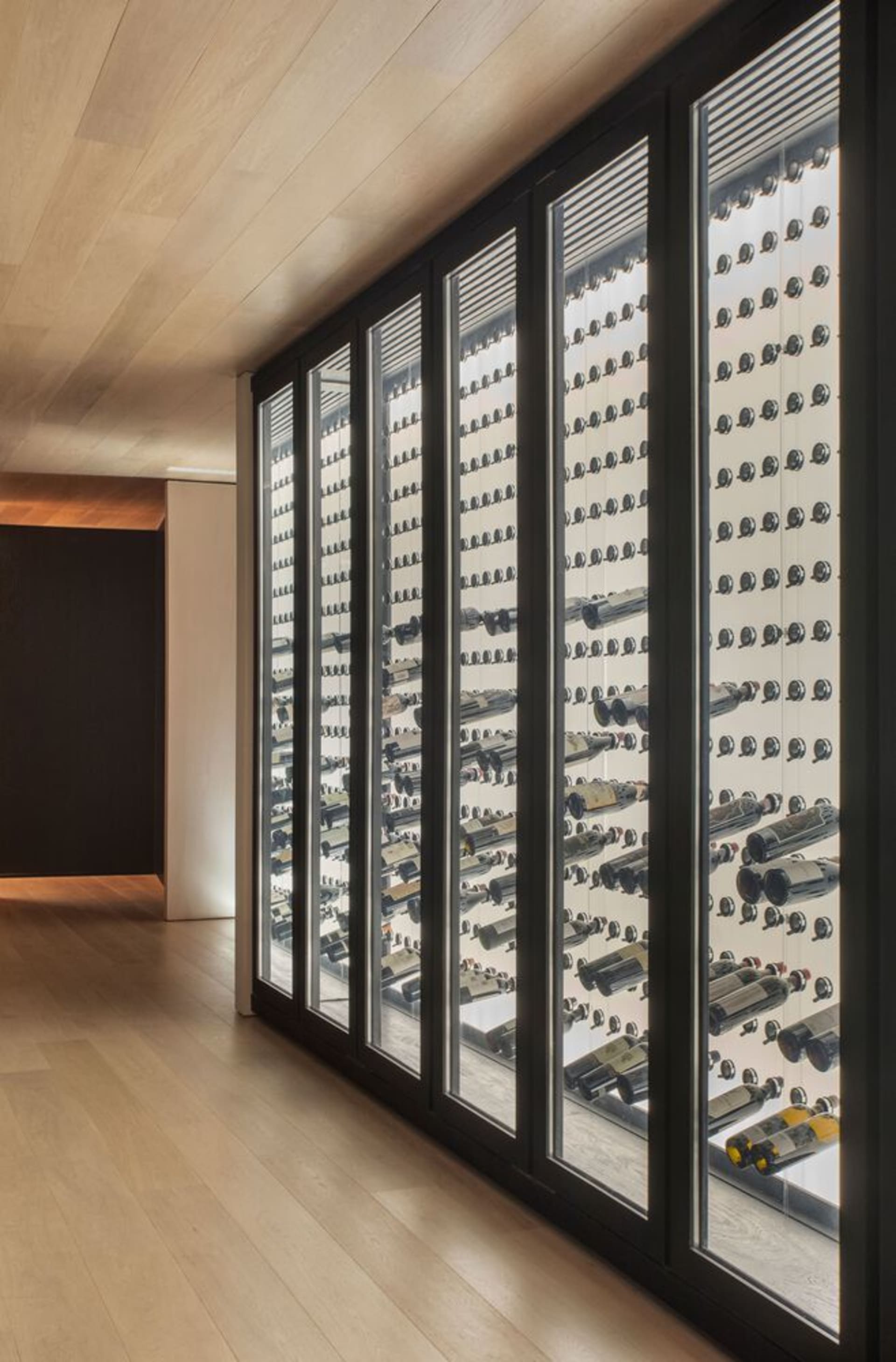 A modern wine cellar with glass doors filled with numerous bottles of wine.