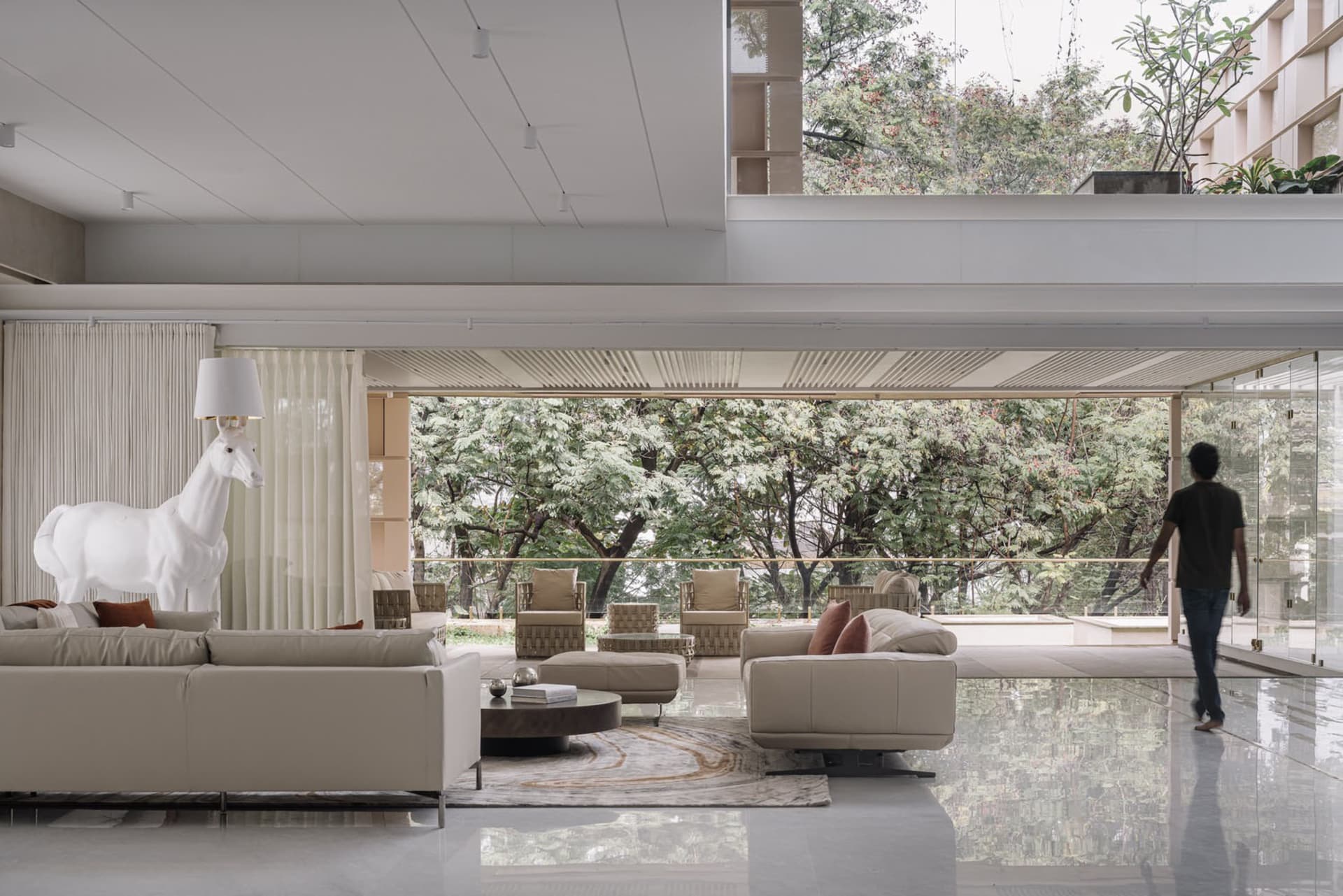 Modern living room with concrete flooring and furniture, large windows showing greenery, and minimalist design.