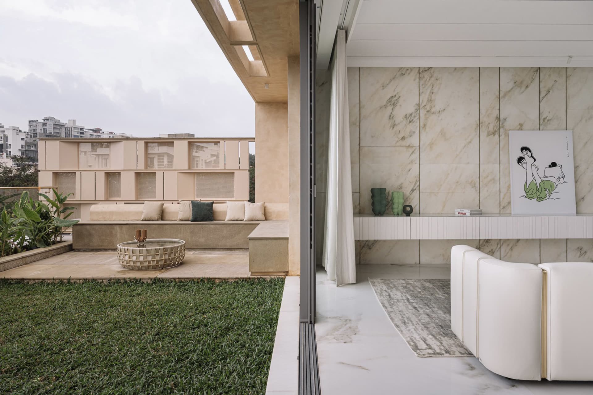A minimalist living room featuring marble flooring and walls, with a white sofa and green plants on a small patio.