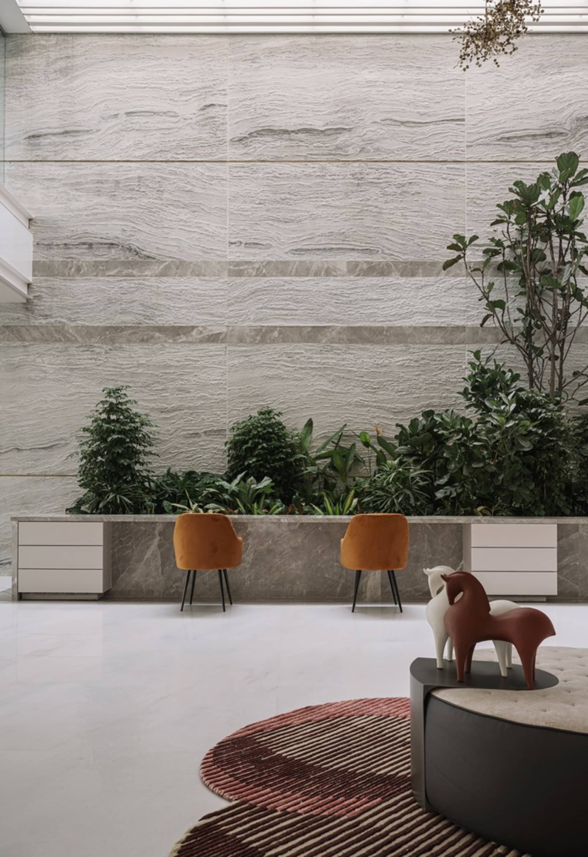 A modern lounge area with marble walls, plants, and plush seats.