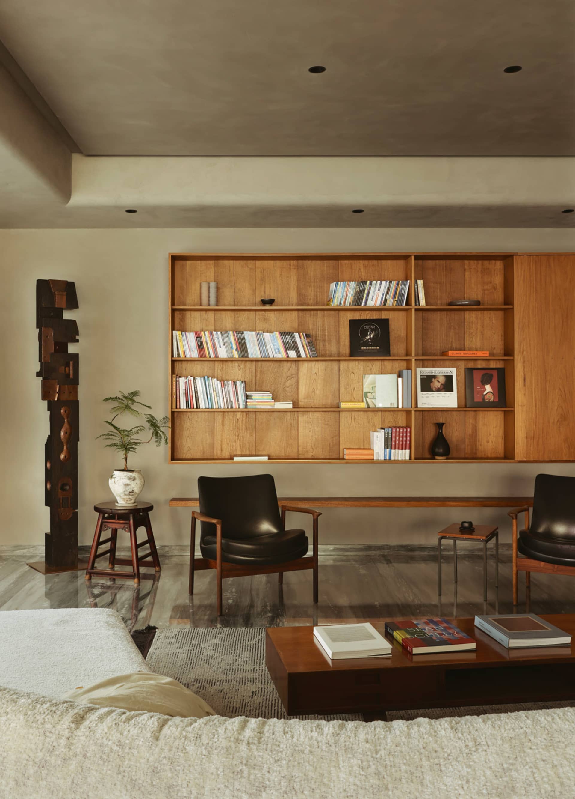A modern living room with wooden shelves, leather chairs, and concrete flooring.