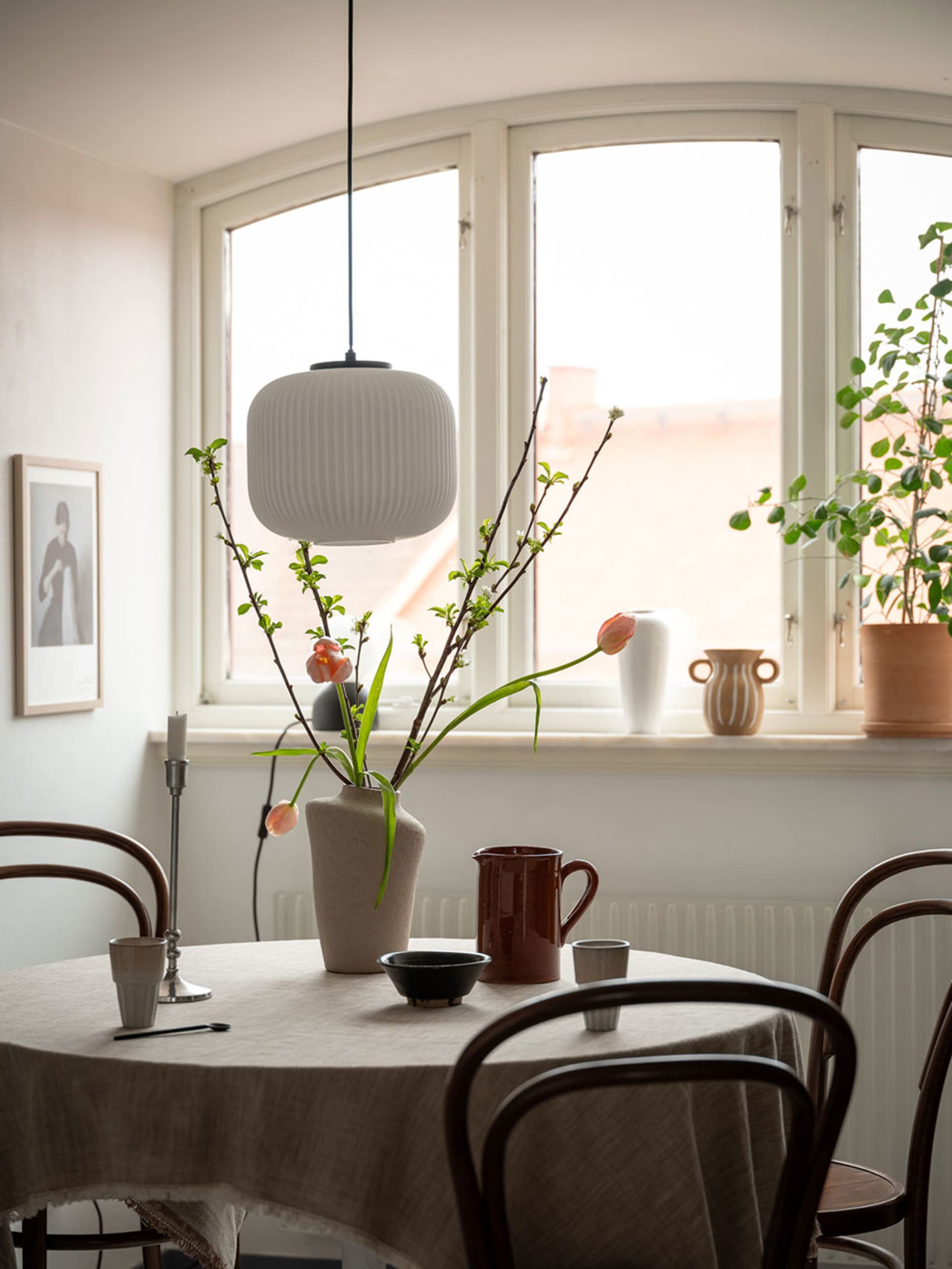 A cozy kitchen scene featuring a ceramic vase with branches and tulips, a mix of ceramic dishes, and soft lighting from a pen