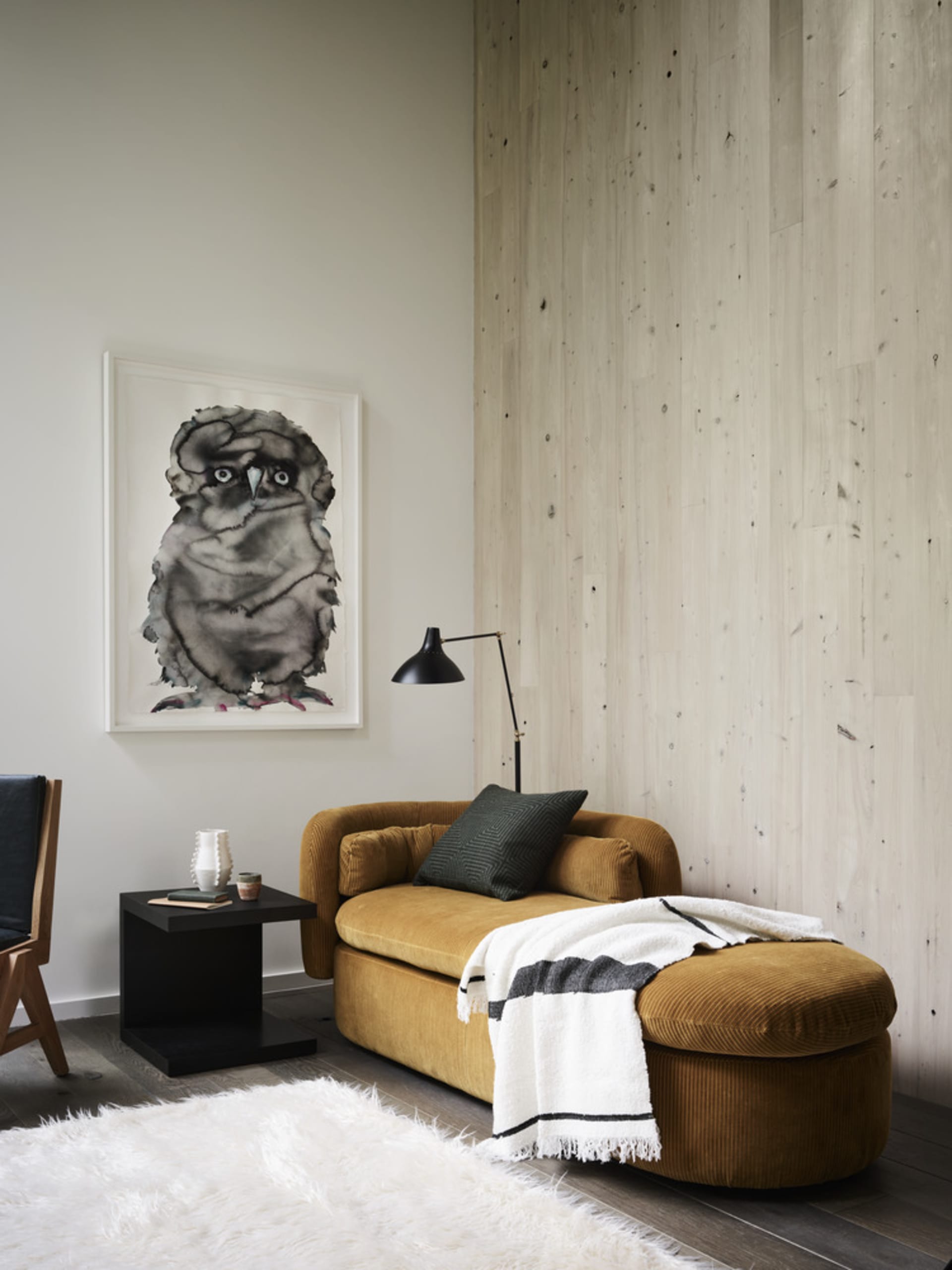 A modern living room with a comfortable mustard-colored sofa, a black floor lamp, a framed picture of an owl, a small black s