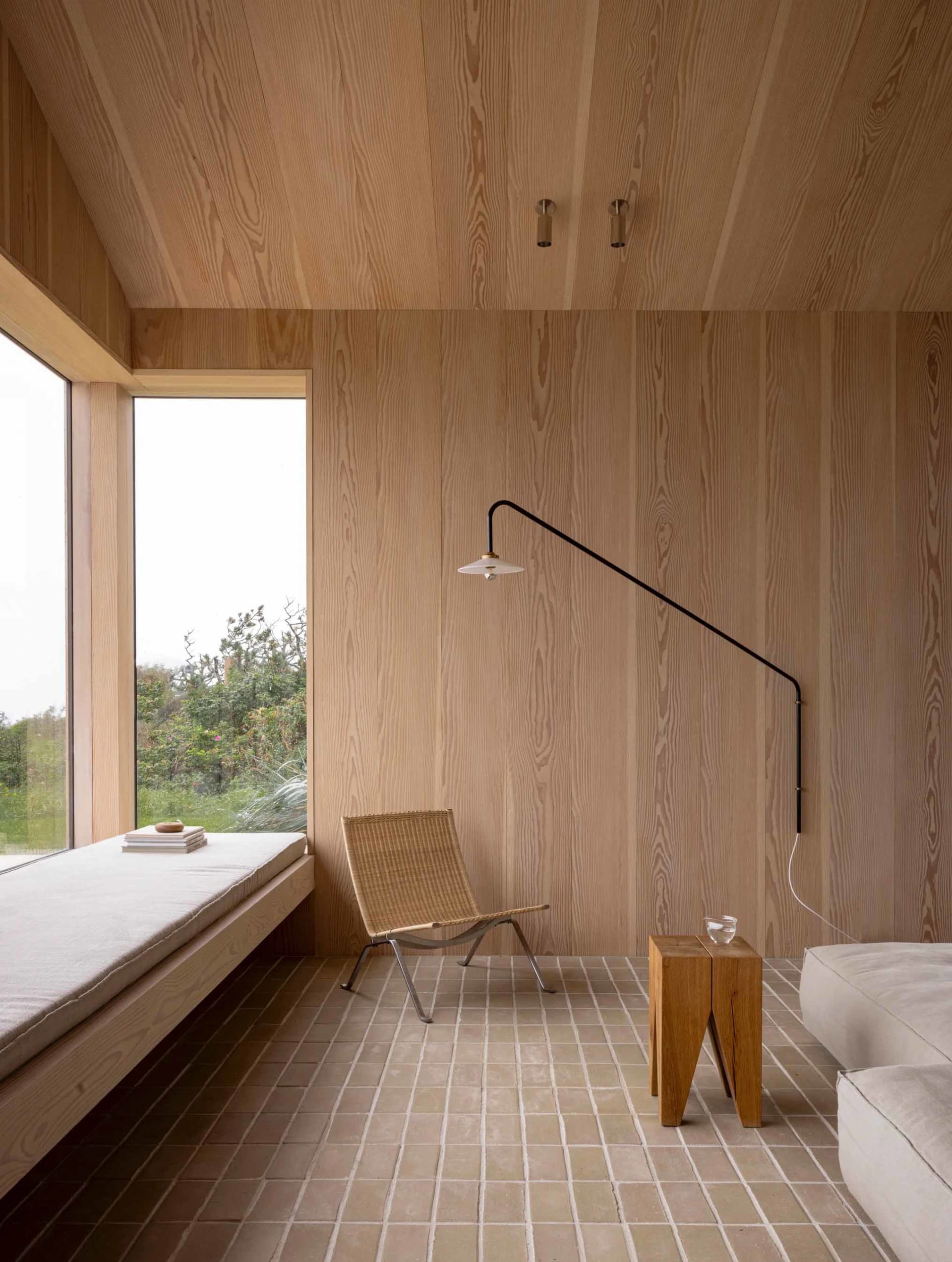 A minimalist living room featuring wood-paneled walls and a window seat with a wicker chair.