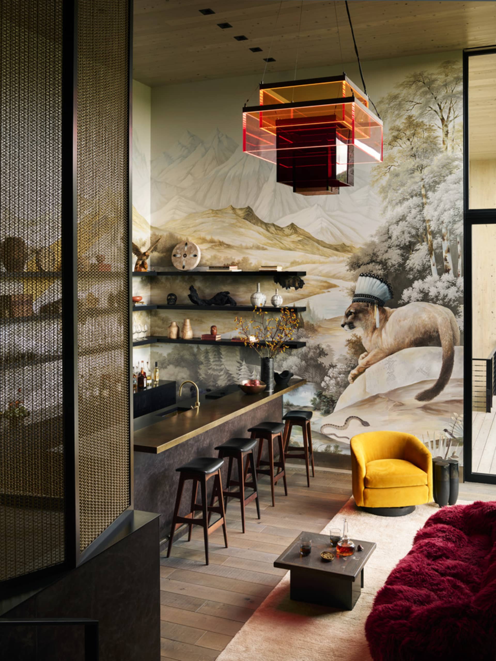 A modern living room bar featuring a yellow chair, red sofa, and a mountain mural backdrop.