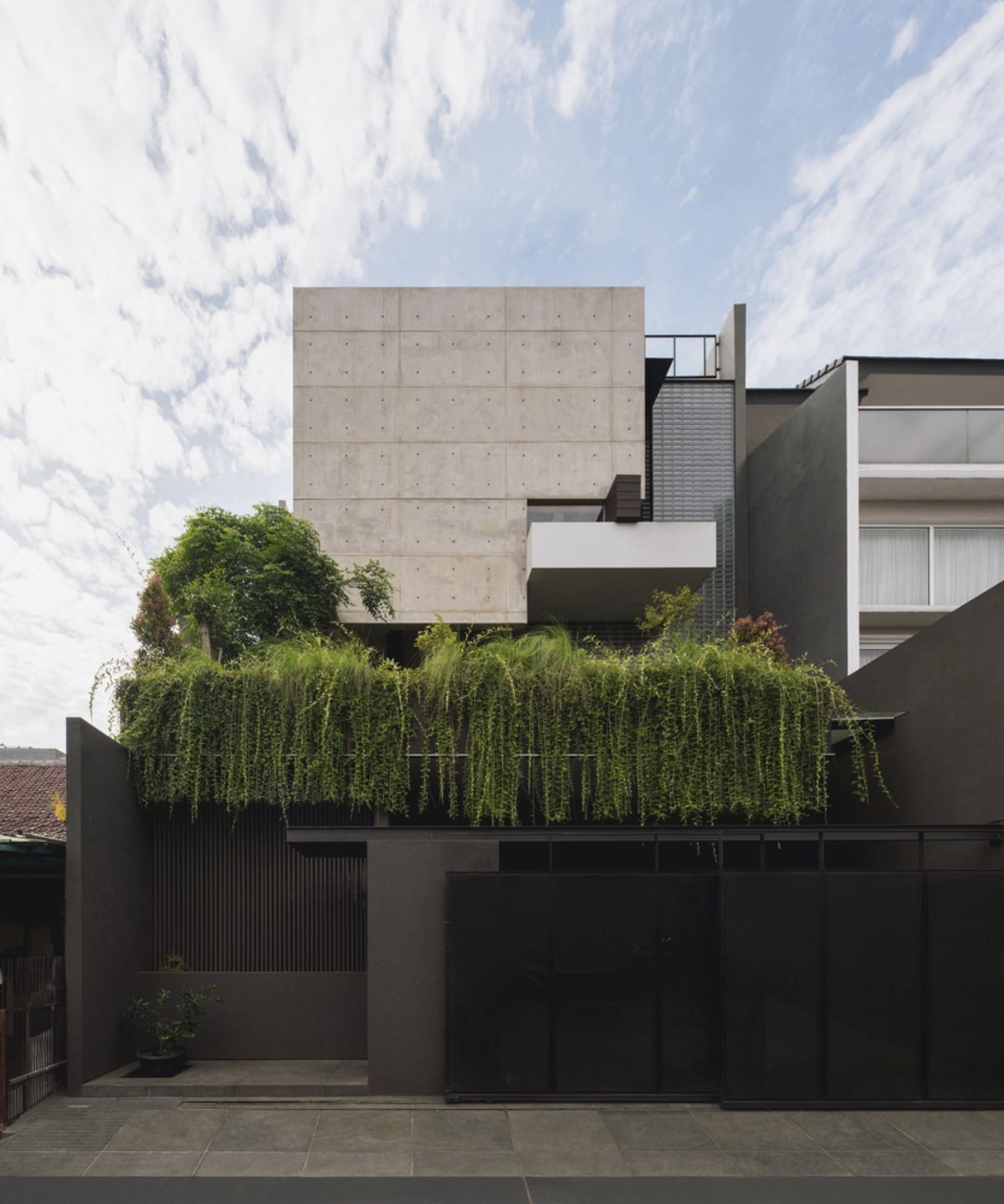 Modern, minimalist concrete house exterior with greenery on the rooftop.