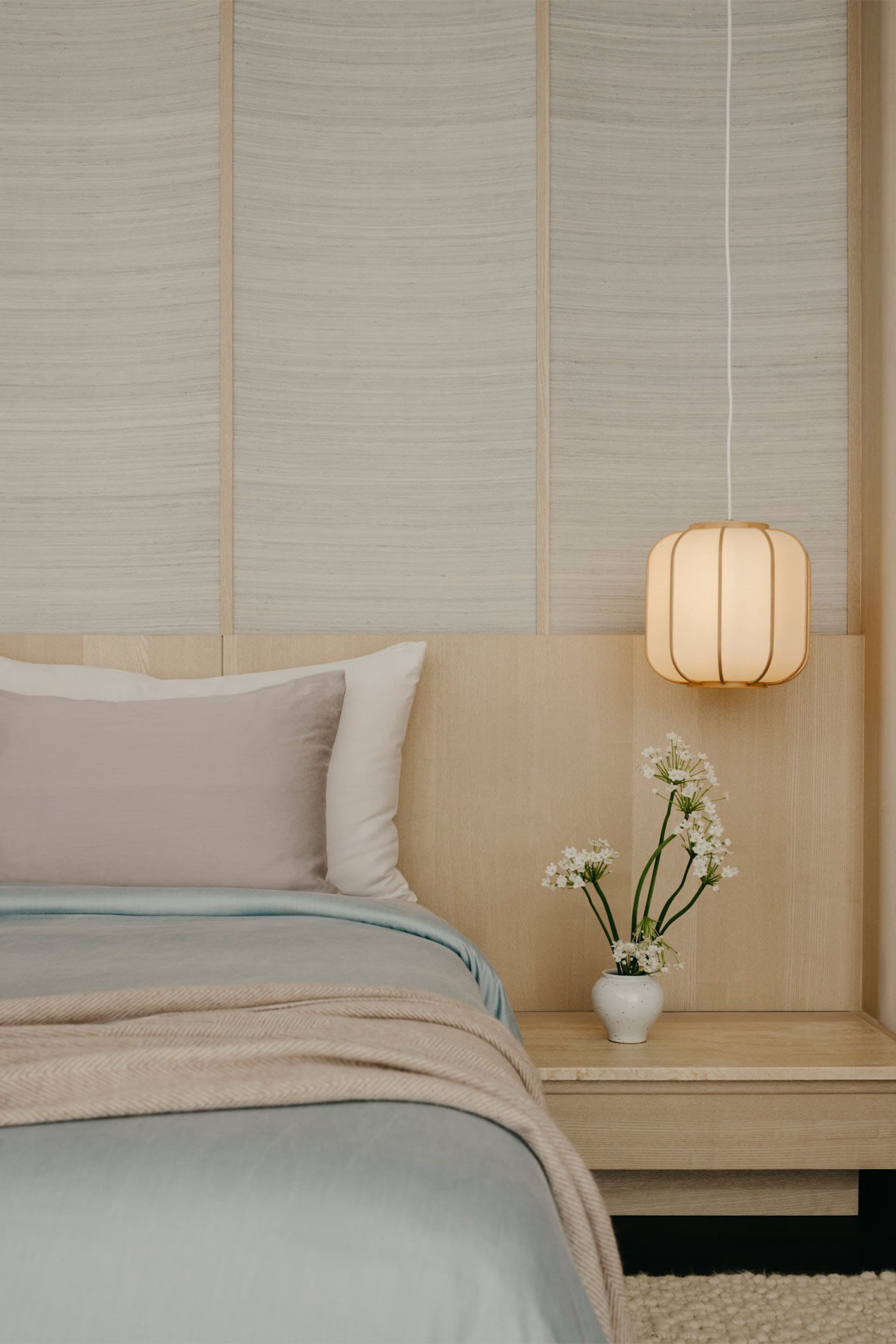 A minimalist bedroom with a bed, pillows, and a hanging lamp with flowers on a nightstand.