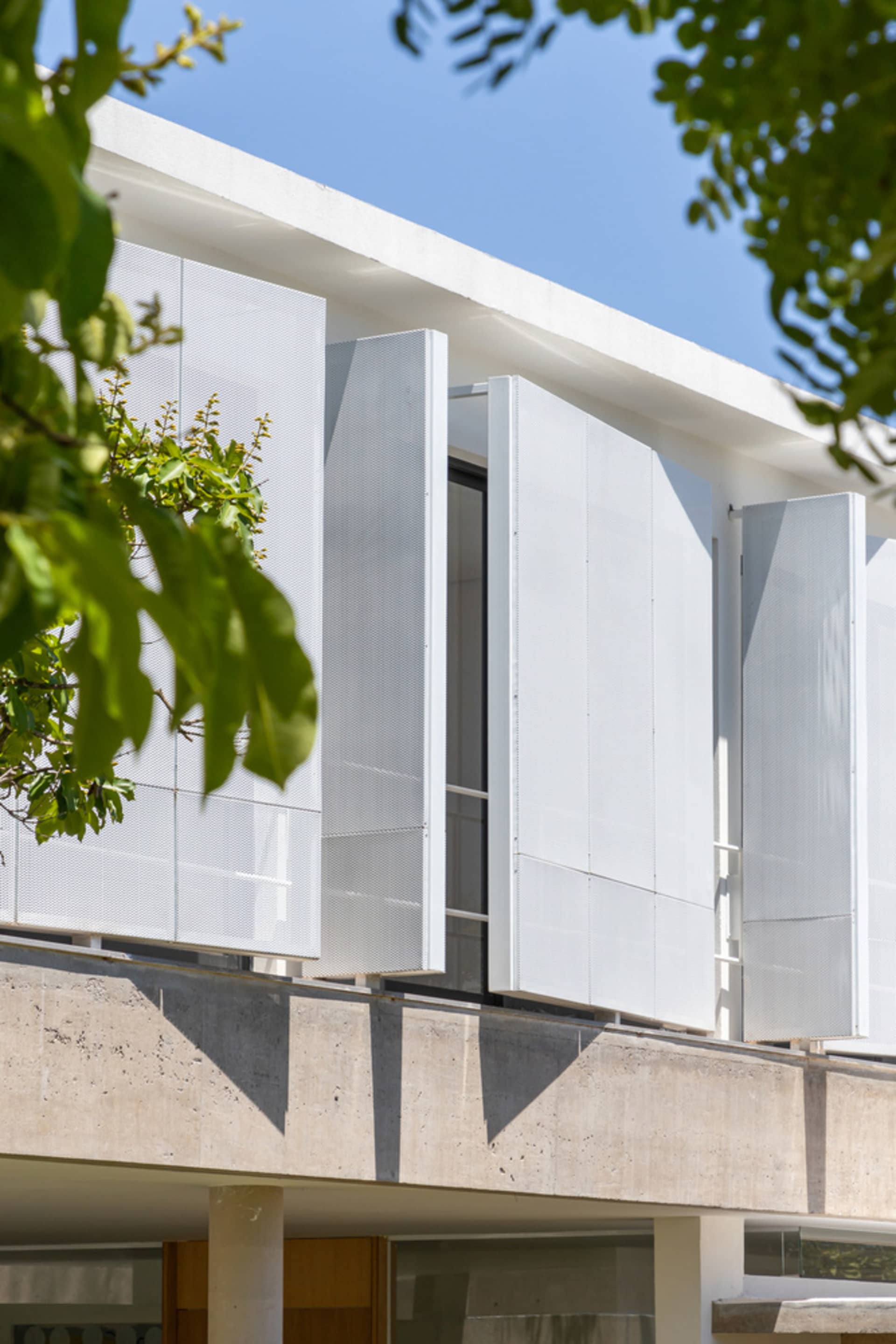 White perforated metal panels on a modern building facade under a clear blue sky.
