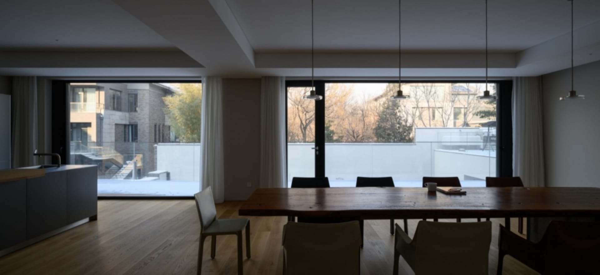 Modern residential dining room featuring a wooden dining table and glass walls overlooking a snowy courtyard.