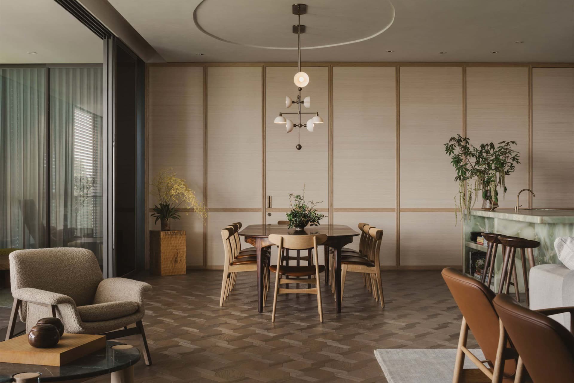 A modern dining room featuring wooden furniture and countertops, with a chandelier and plants.