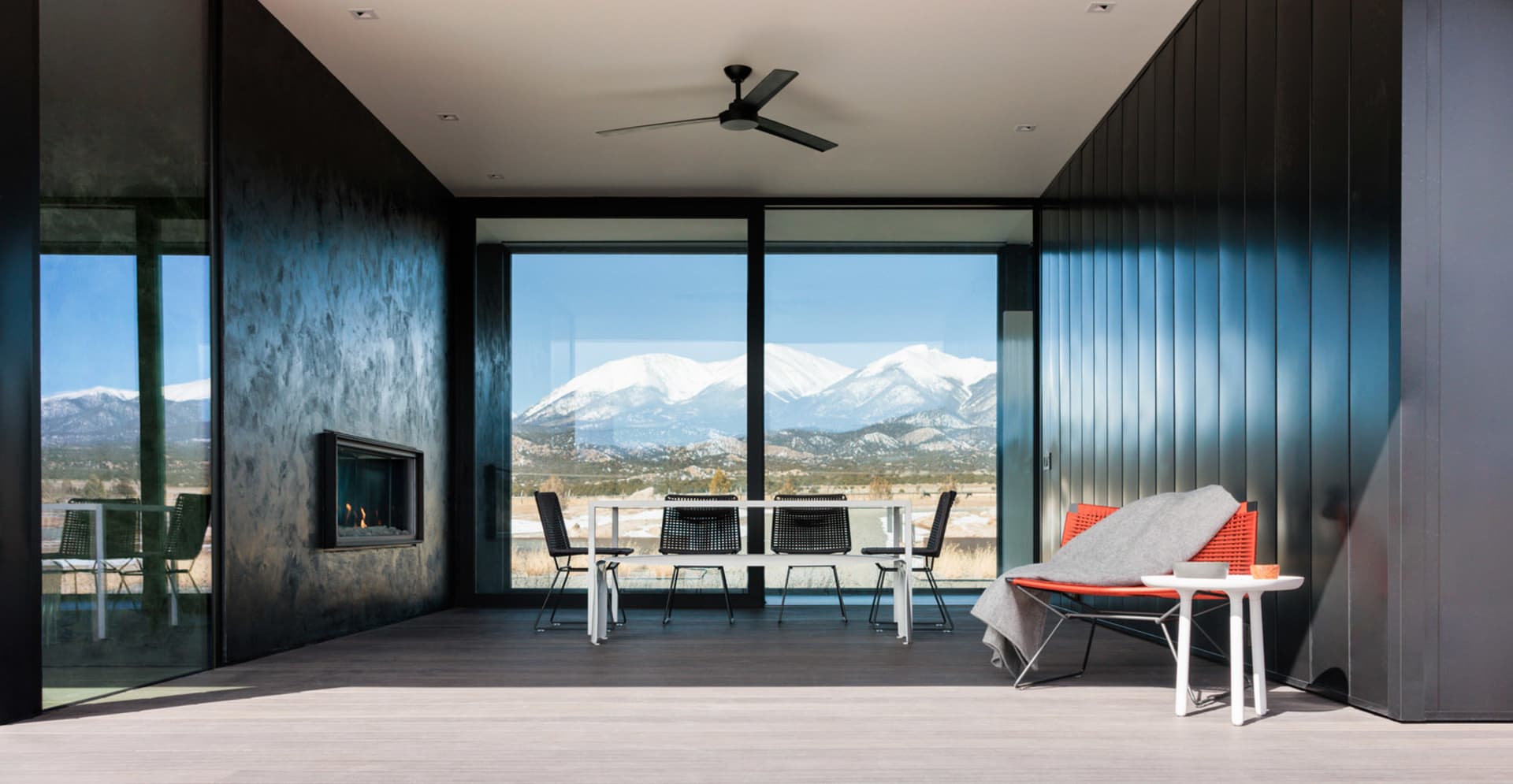Modern living room featuring black-framed windows overlooking snowy mountains.