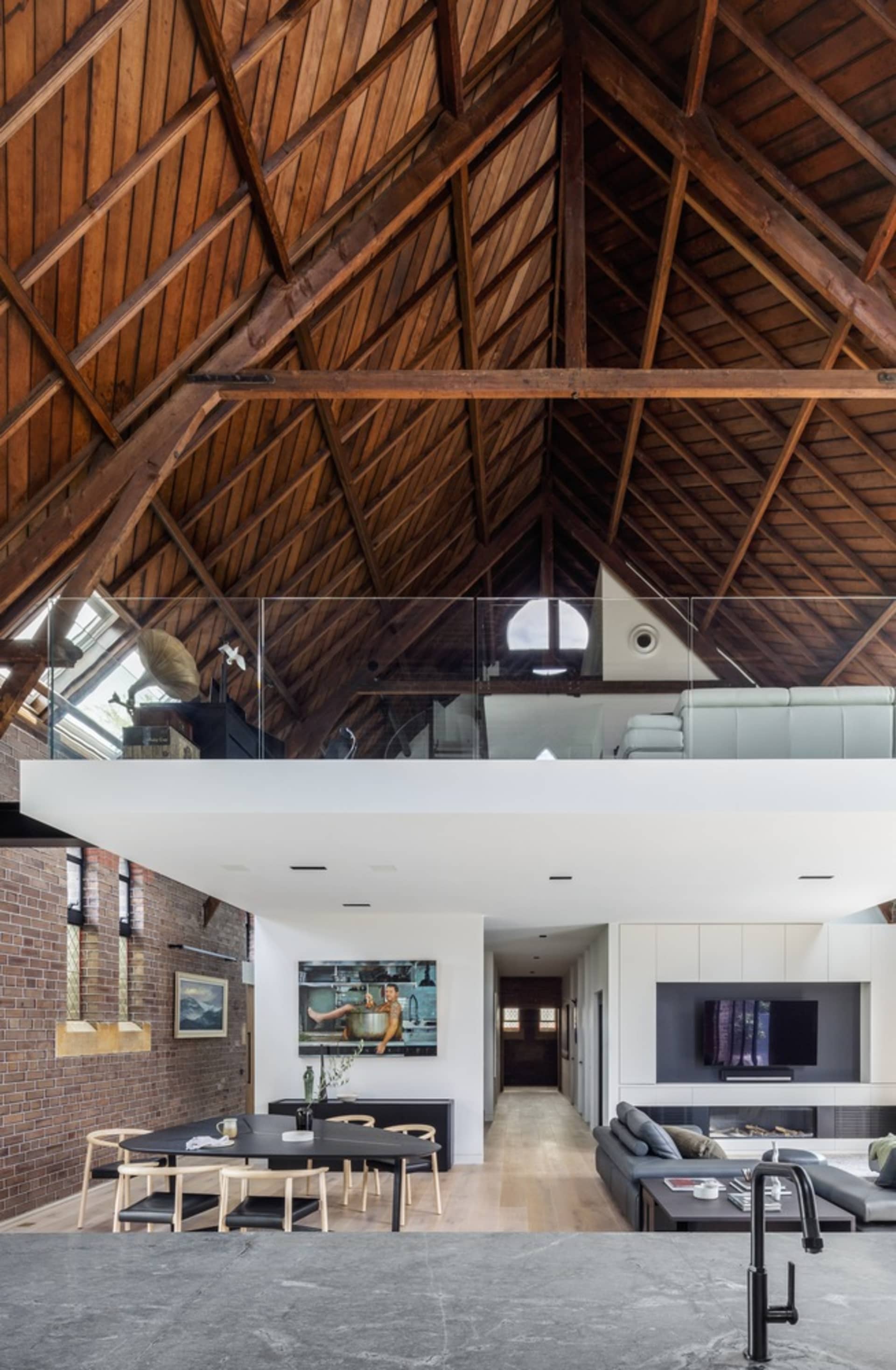 Modern living room with wooden accents, featuring a high ceiling with exposed beams and a cozy seating area.