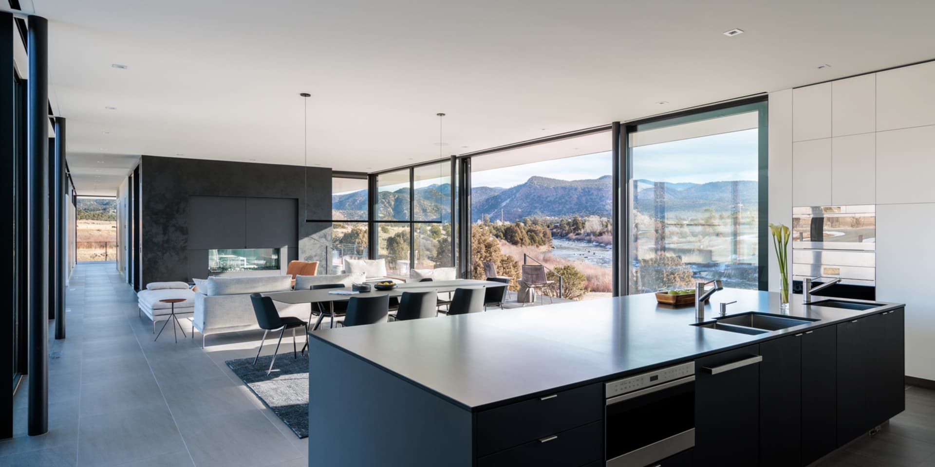 Modern kitchen featuring a large island with a metallic countertop, glass windows overlooking mountains, and a minimalist des