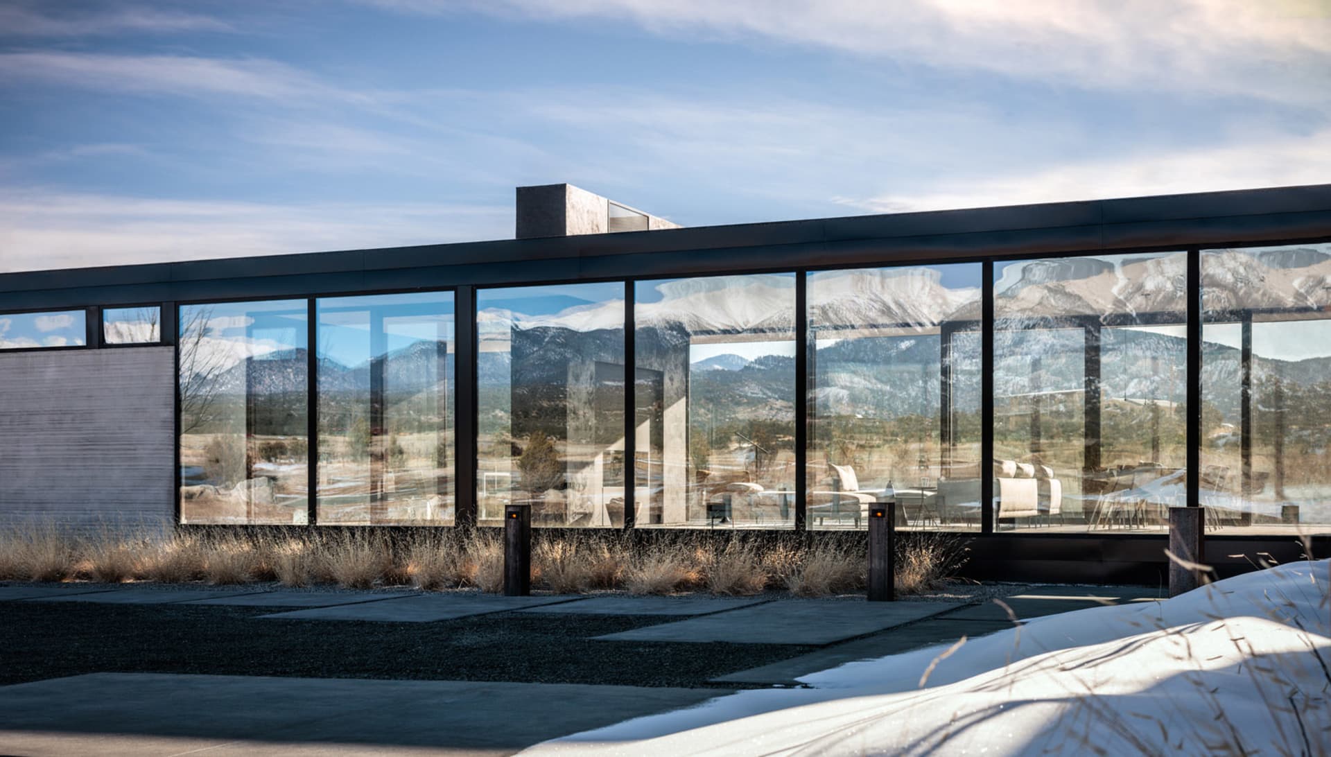 Modern residential home with large glass windows reflecting snow-capped mountains, featuring a sleek design with glass and co