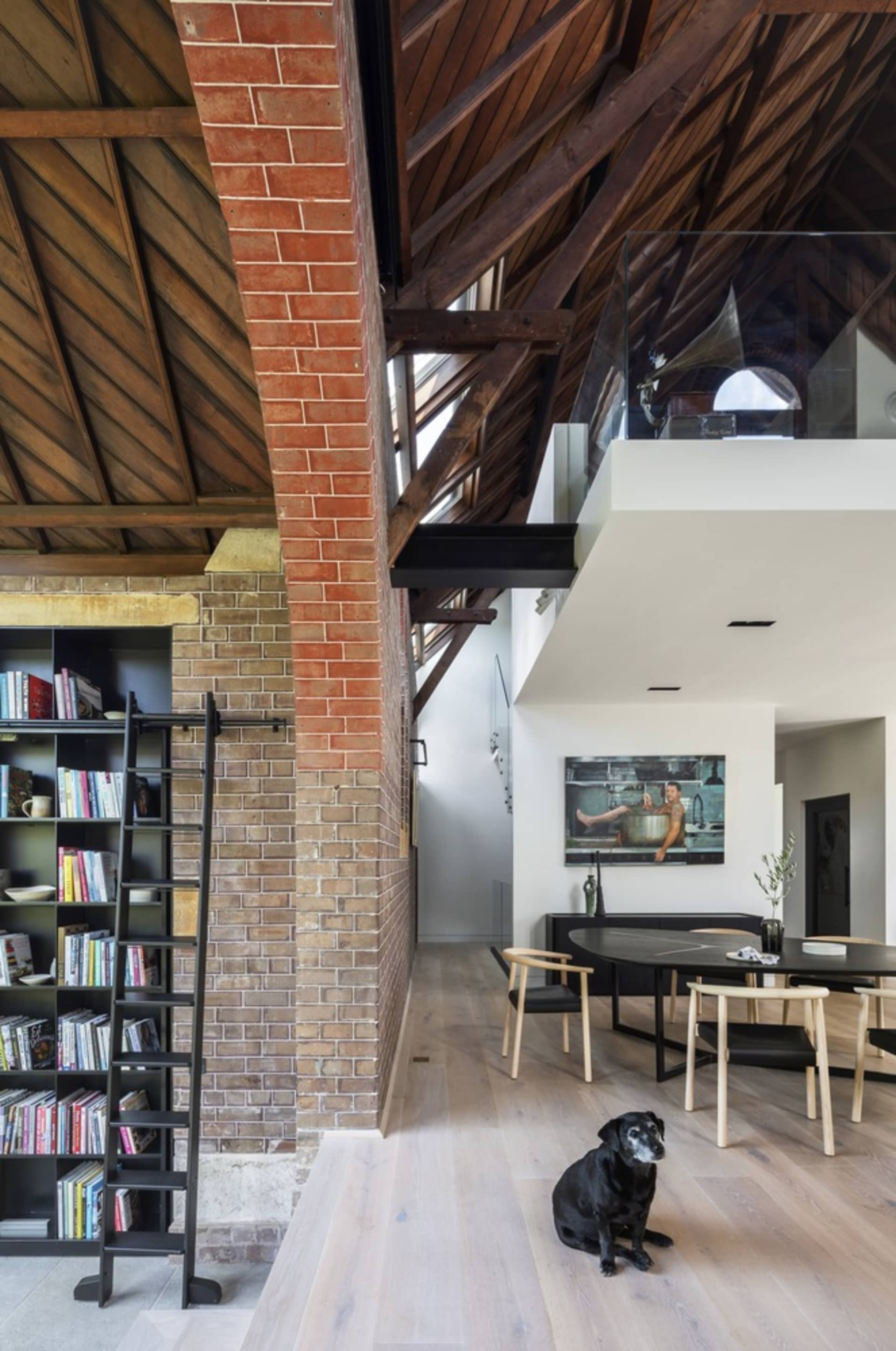 Modern residential space featuring exposed brick, concrete flooring, and wooden beams, with a black and white dog sitting on