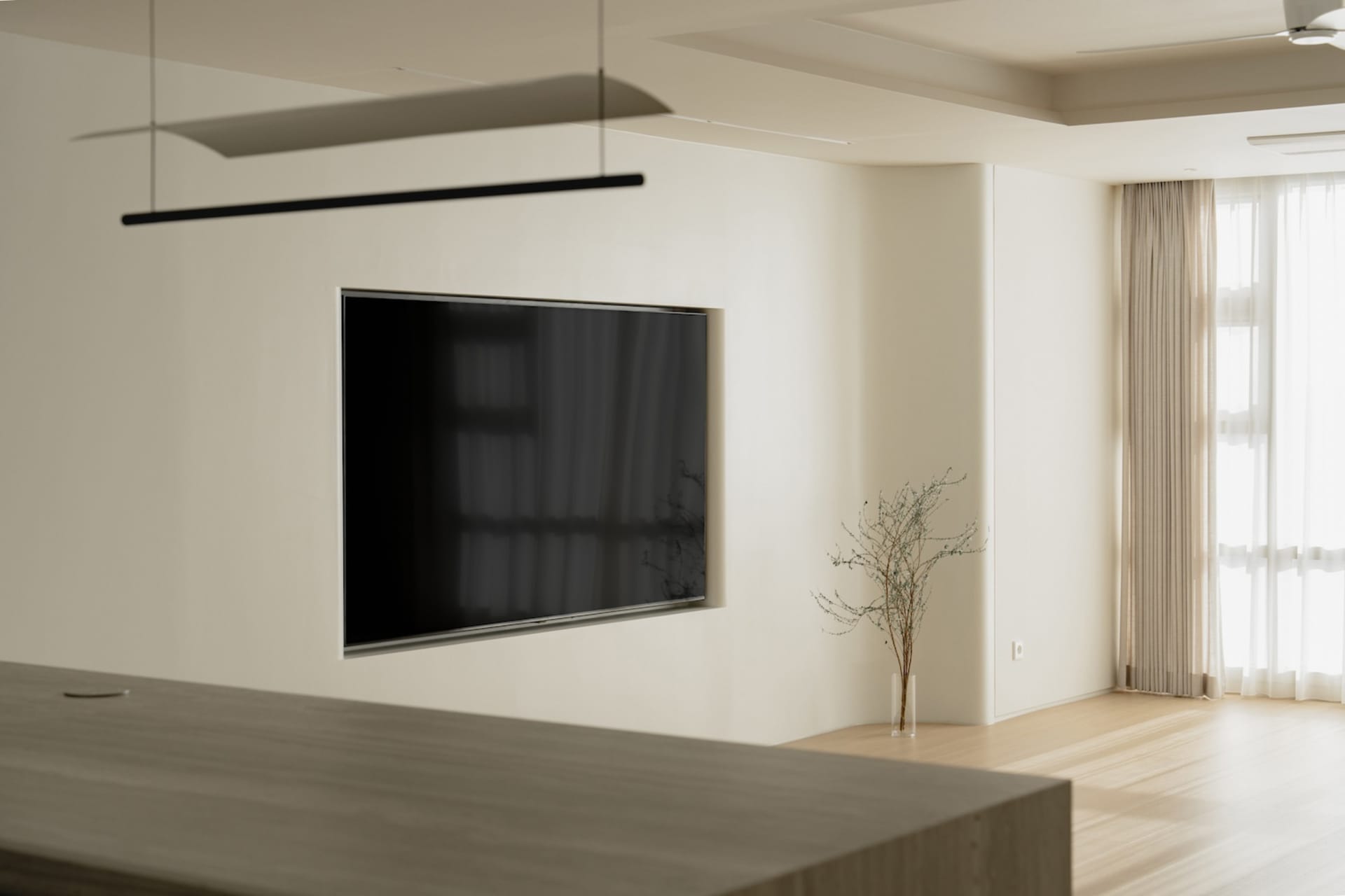Modern living room with neutral-colored walls, minimalistic decor, and a large flat-screen television.