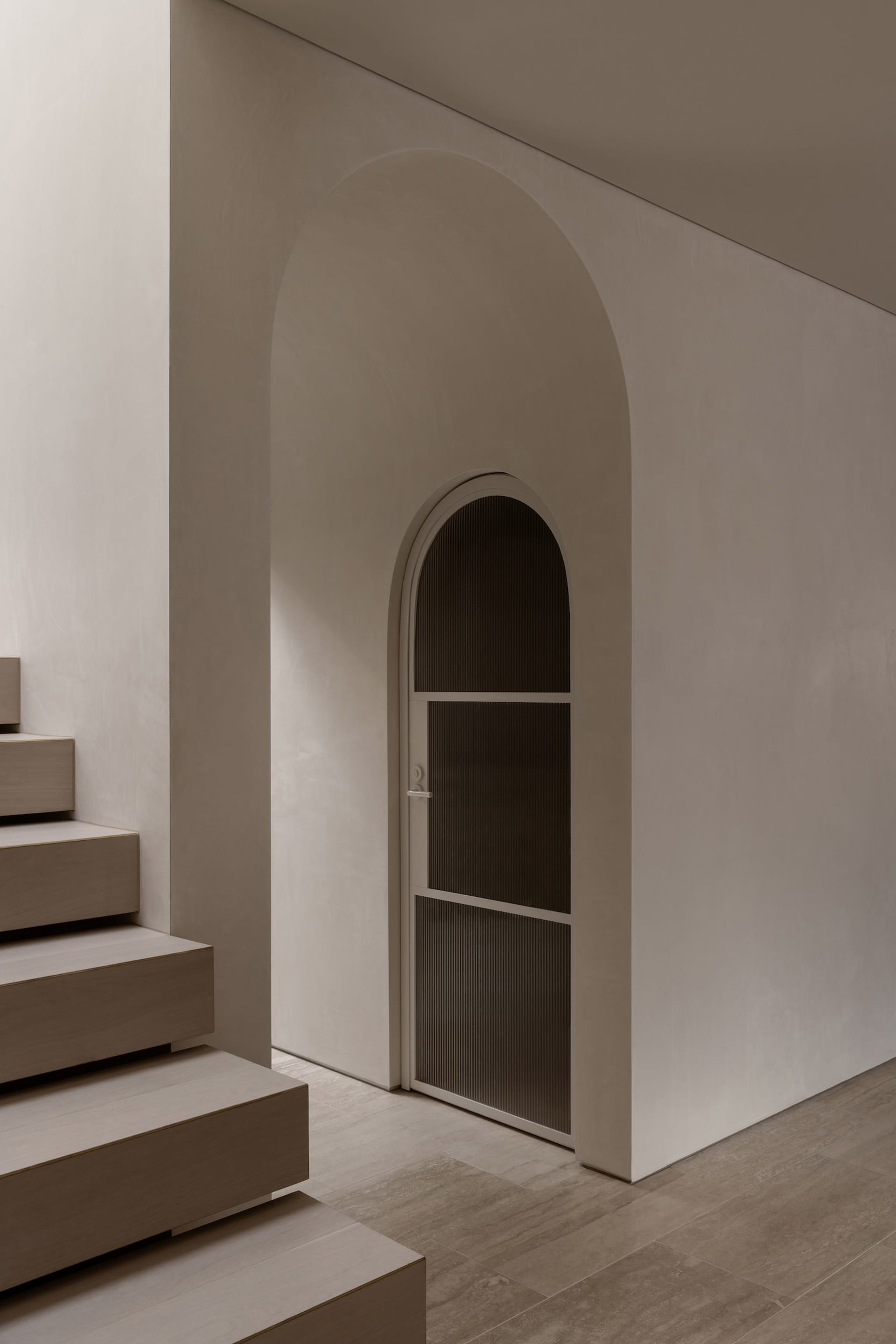 A minimalist entryway featuring concrete stairs and an arched doorway.