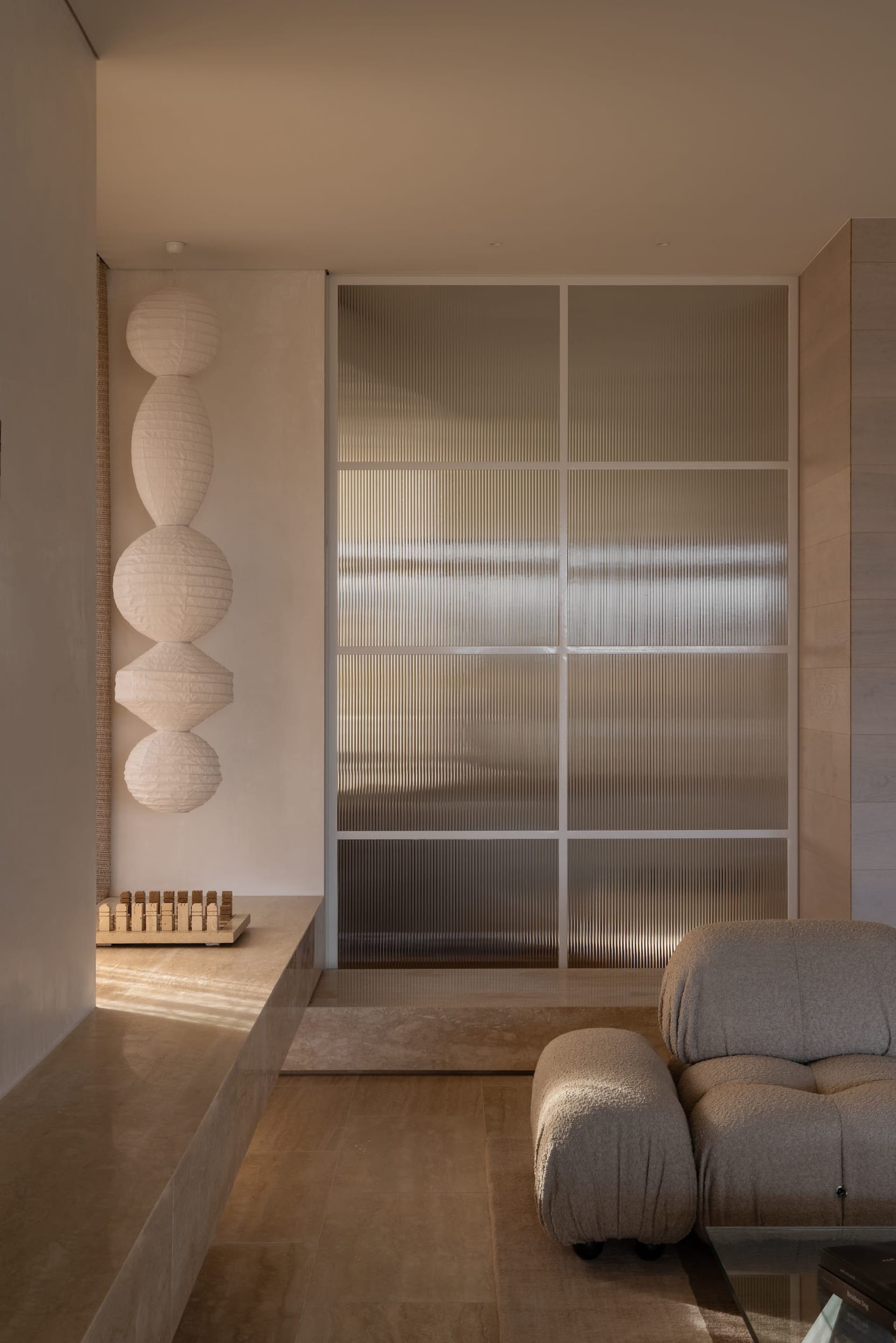Minimalist living room featuring a frosted glass wall, beige sofa, and decorative lamps.