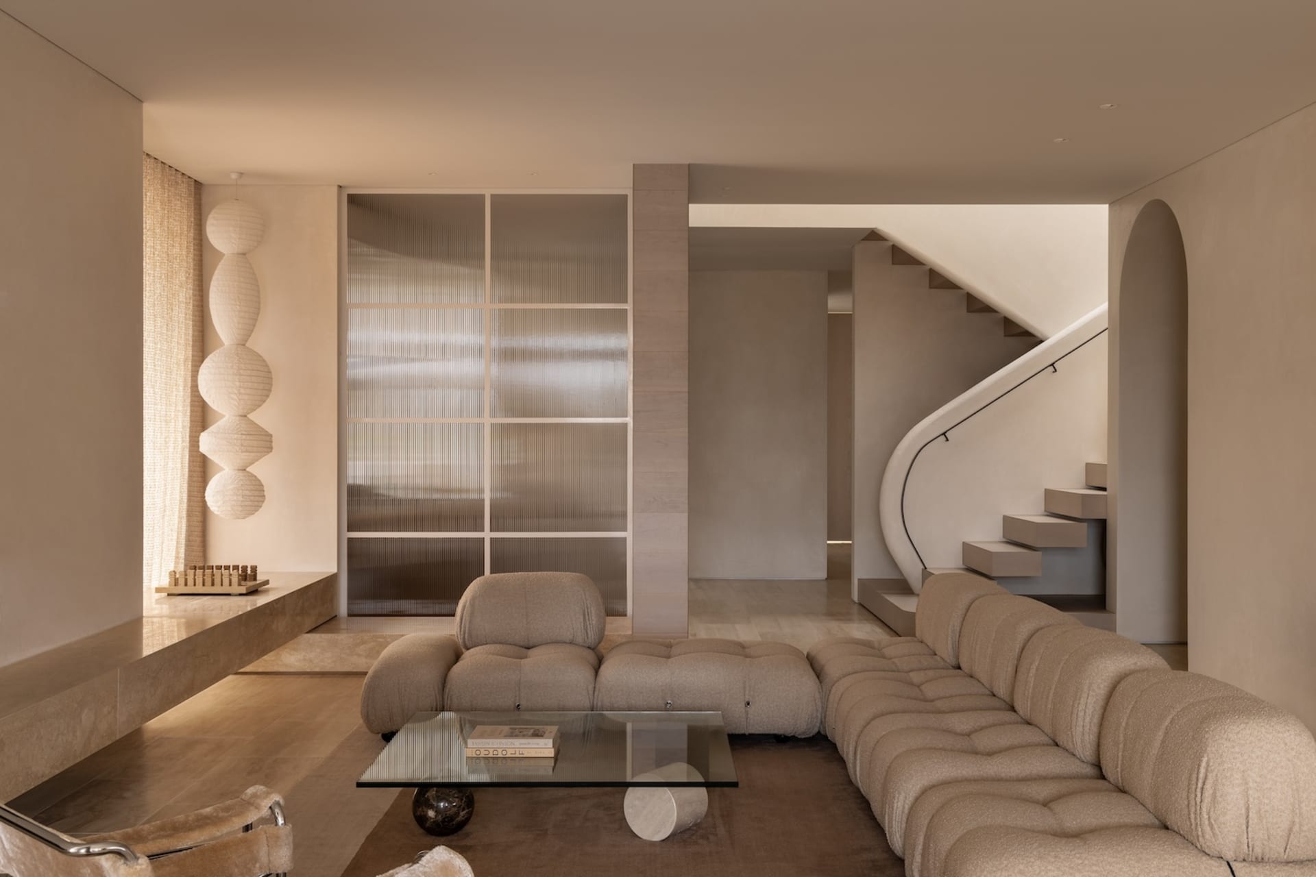 Modern living room with neutral tones, featuring a tufted sofa, glass coffee table, and decorative lighting.