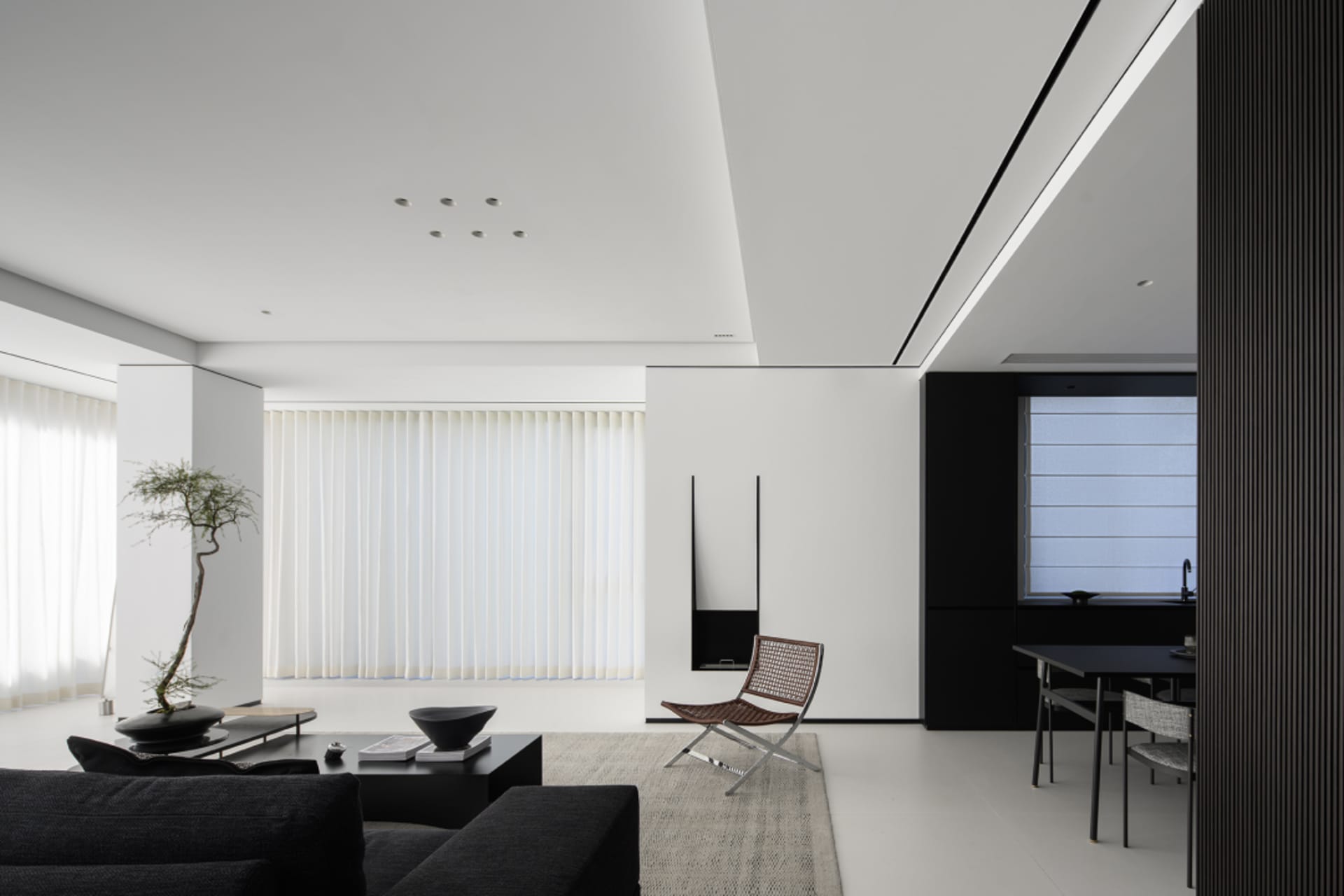 Minimalist living room with white curtains, black furniture, and a small tree.