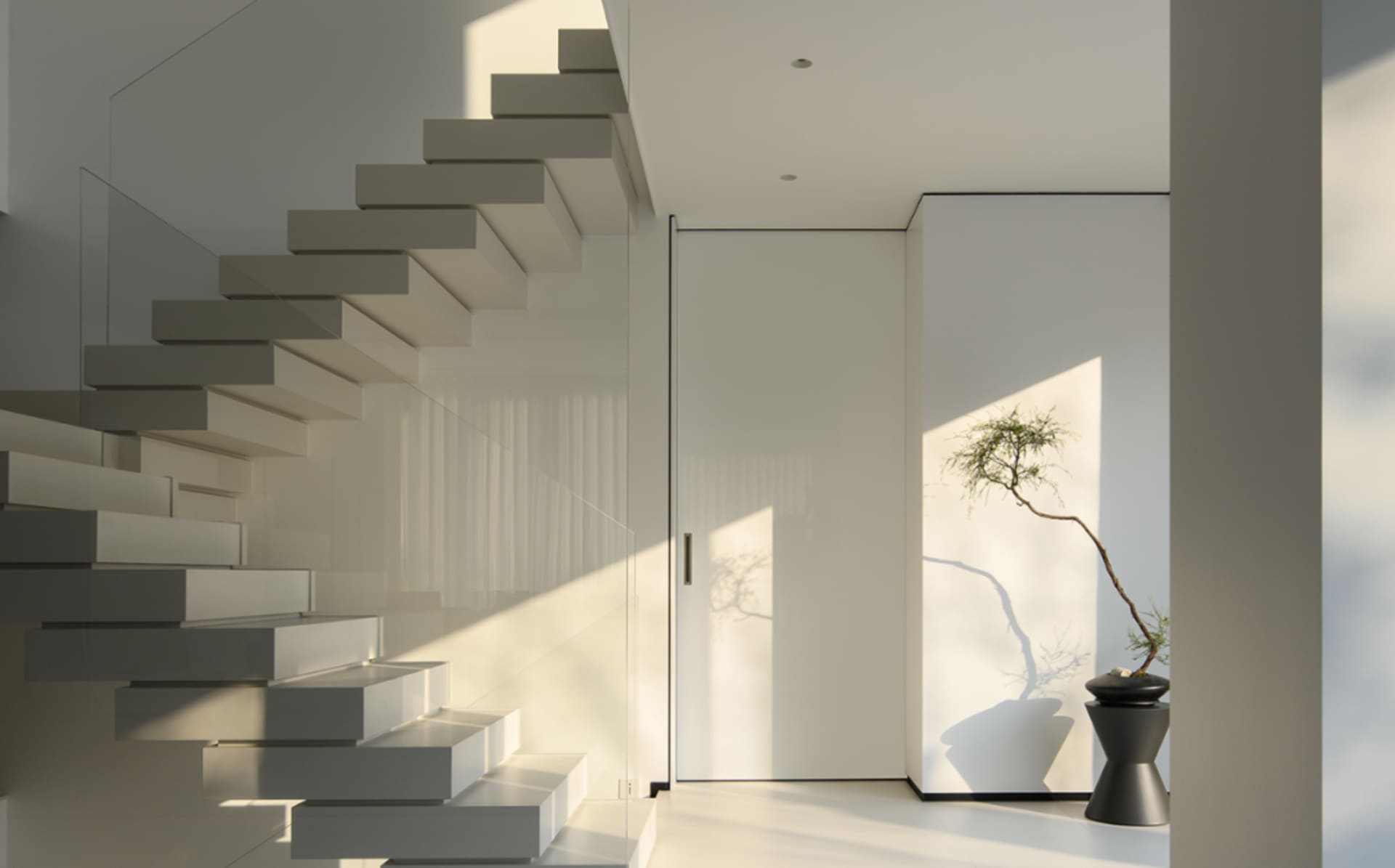 White minimalist interior with glass staircase and door.
