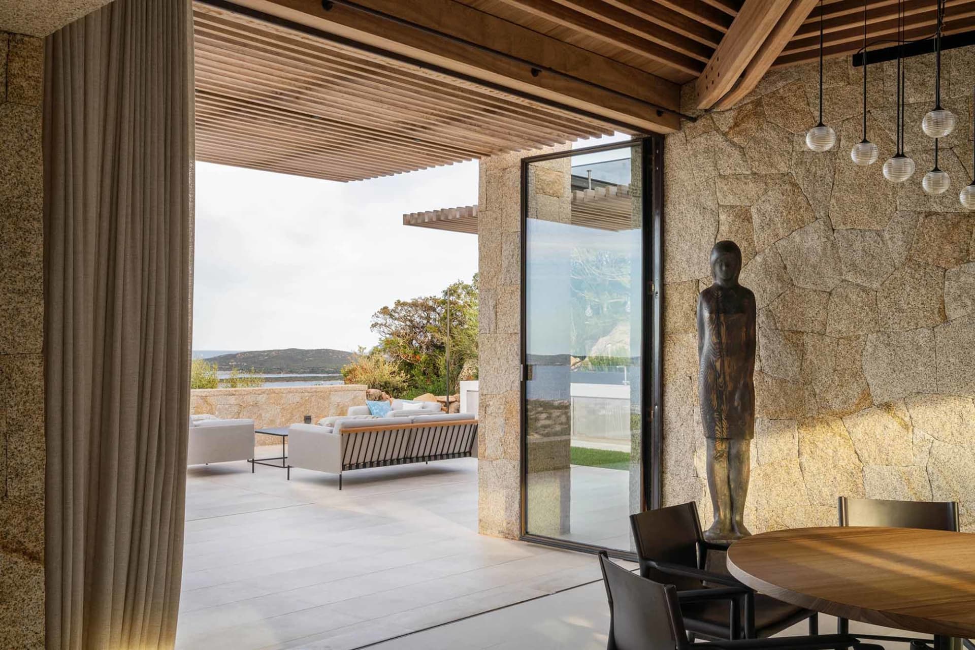 Modern residential exterior featuring granite walls, wooden ceiling beams, and glass doors.