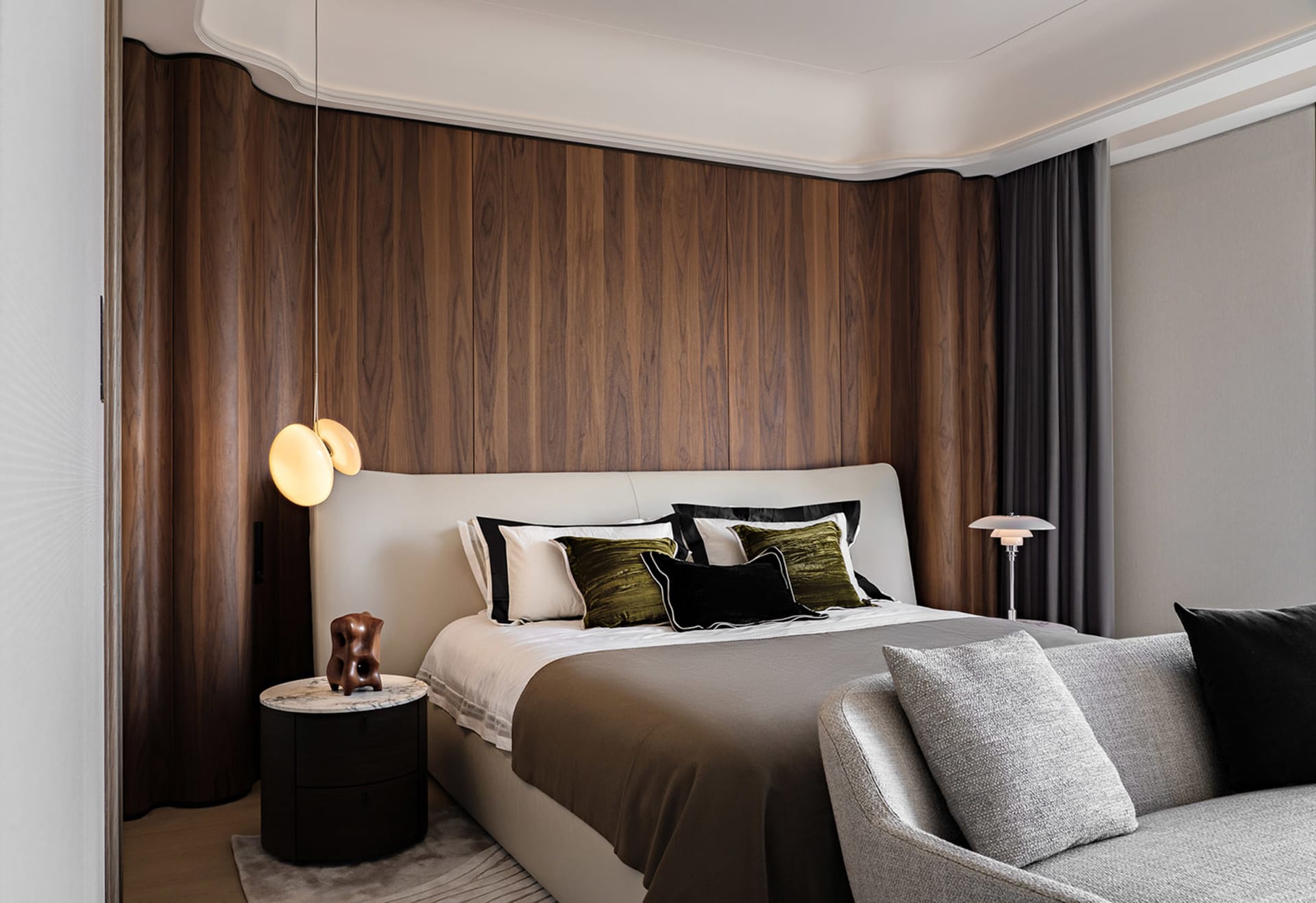 A modern bedroom with a white bed, brown wooden wall panels, and a white sofa.