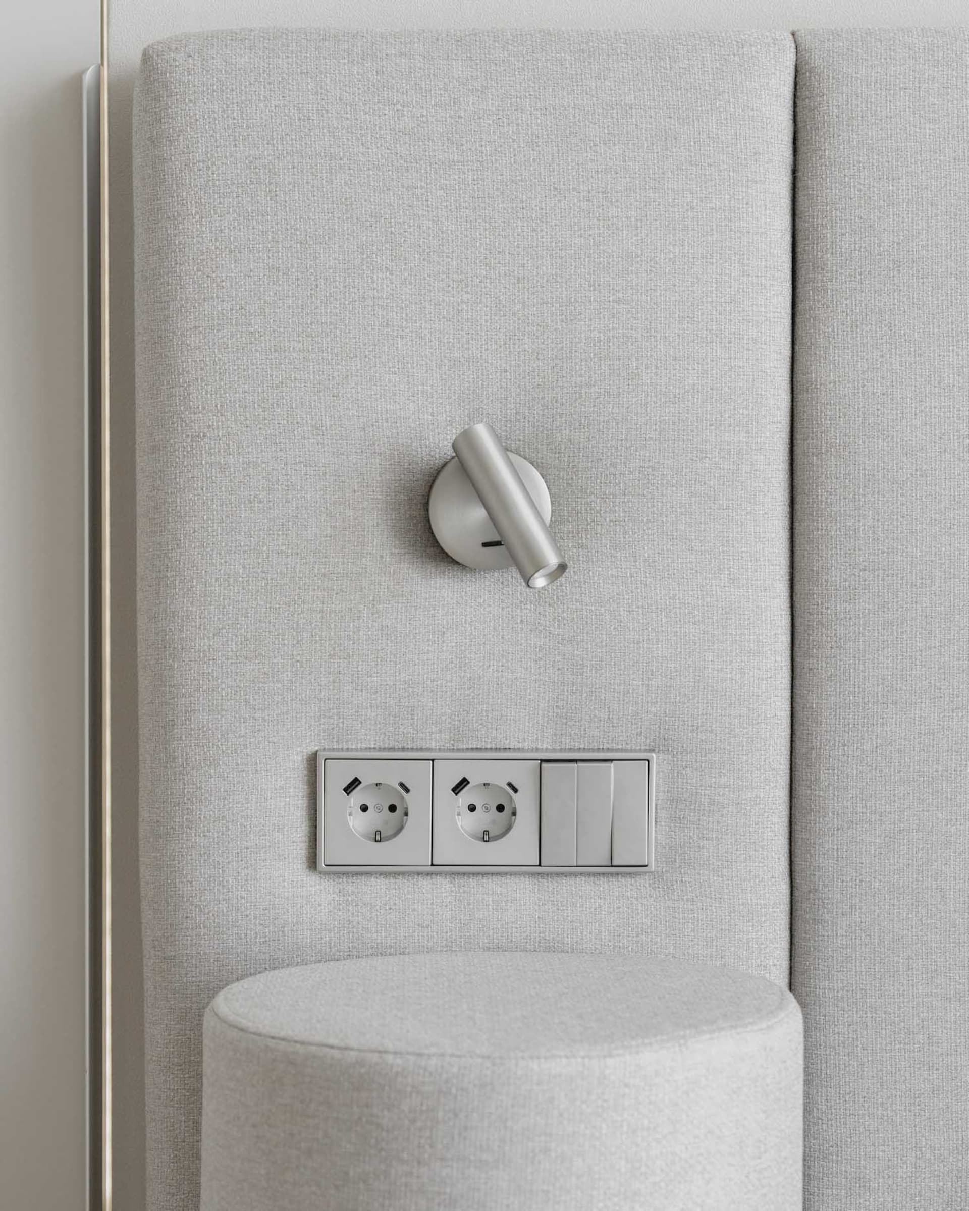 A modern interior wall featuring a light switch, power outlet, and light bulb installed on a neutral fabric wall panel.