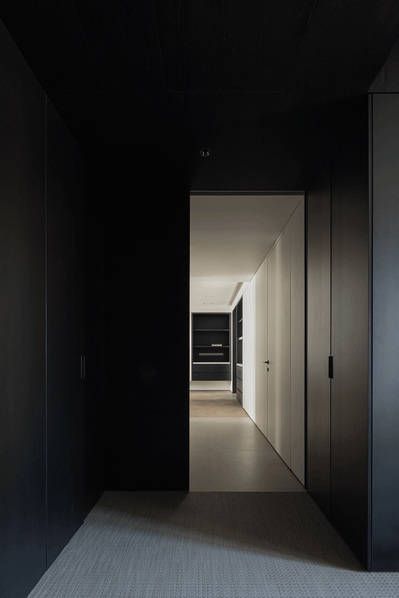 Minimalist interior with black wooden walls and floor, white closet doors, and wooden shelves.