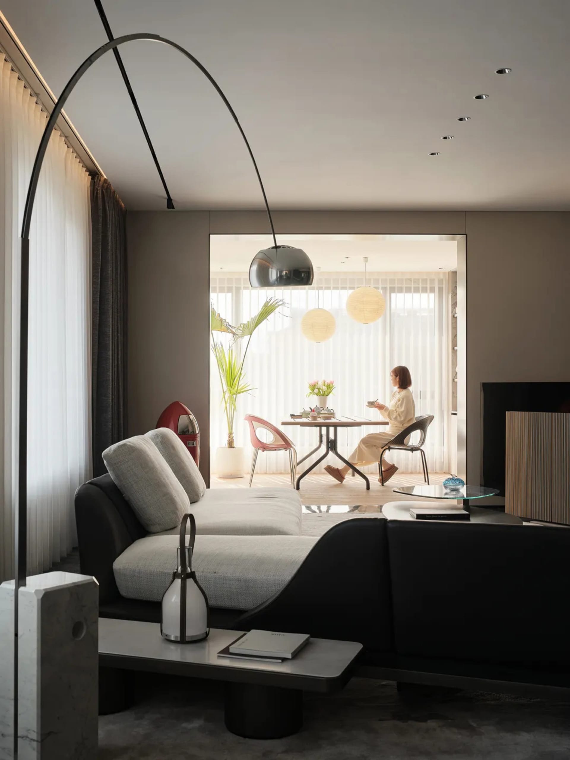 A modern, minimalist living room with a white sofa, black coffee table, and floor-to-ceiling windows.