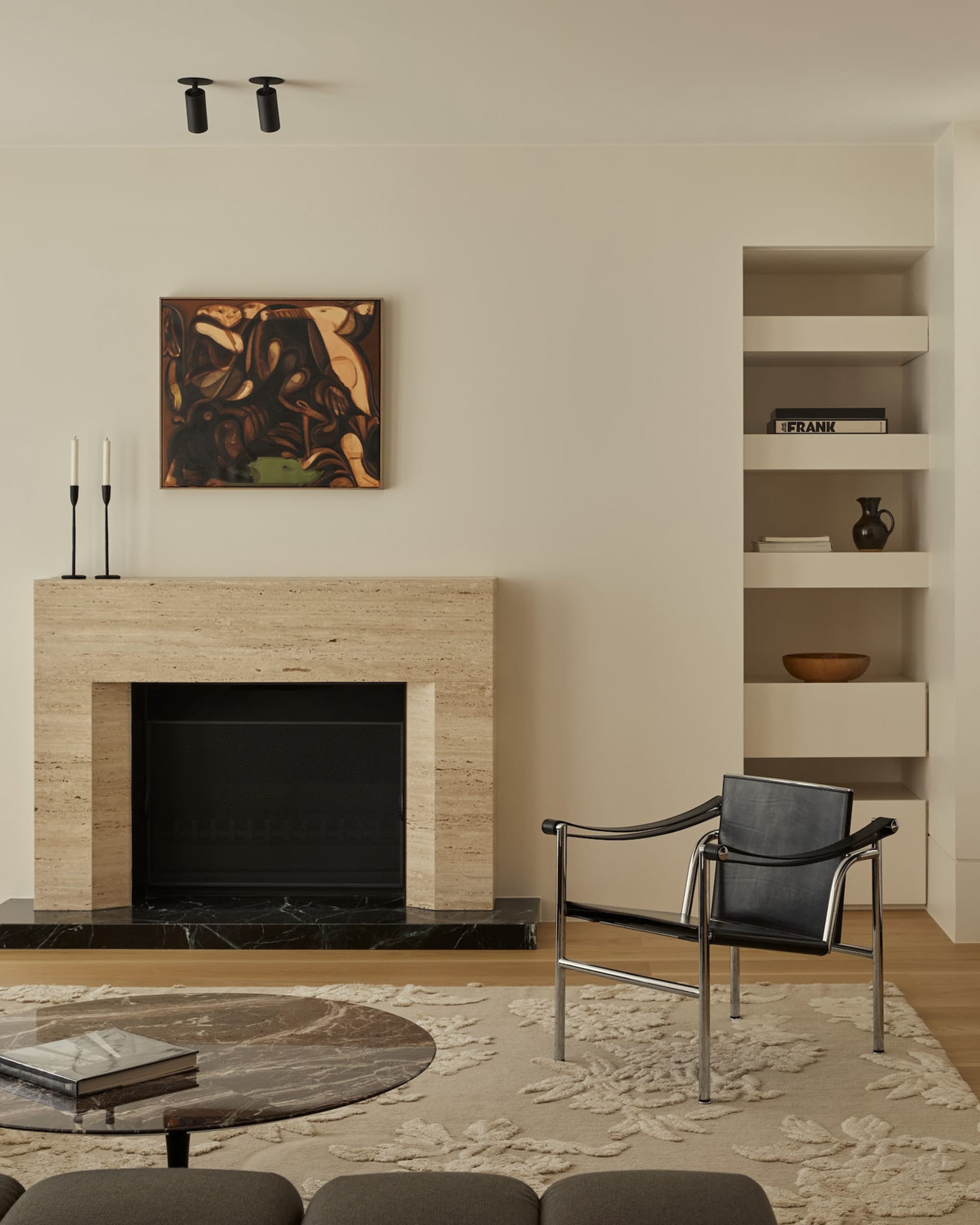 A minimalist living room features a marble fireplace and coffee table, a black leather armchair, and a round marble coffee ta