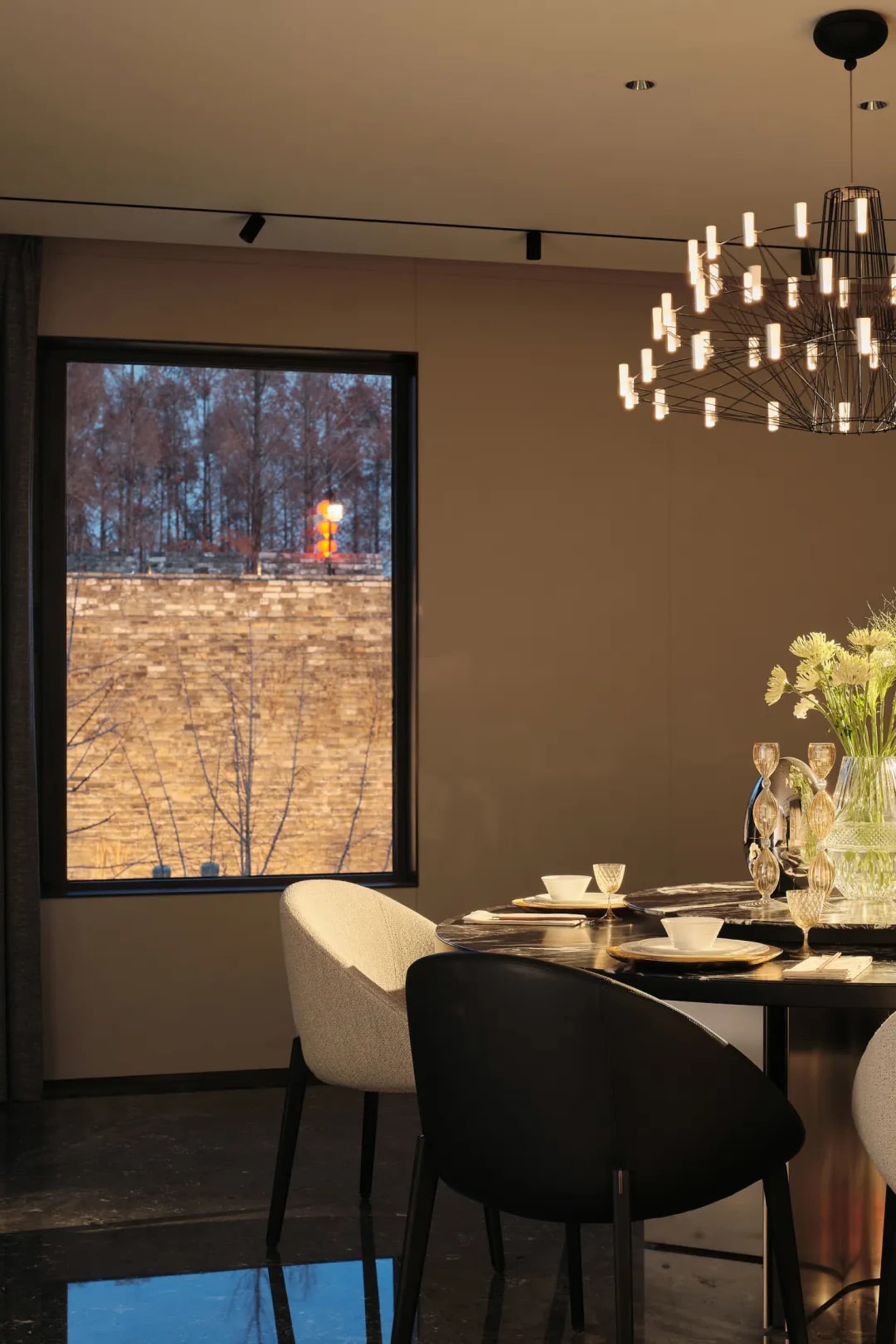 A modern dining room featuring minimalist furniture, a round table with a minimalist chandelier, and a large window overlooki