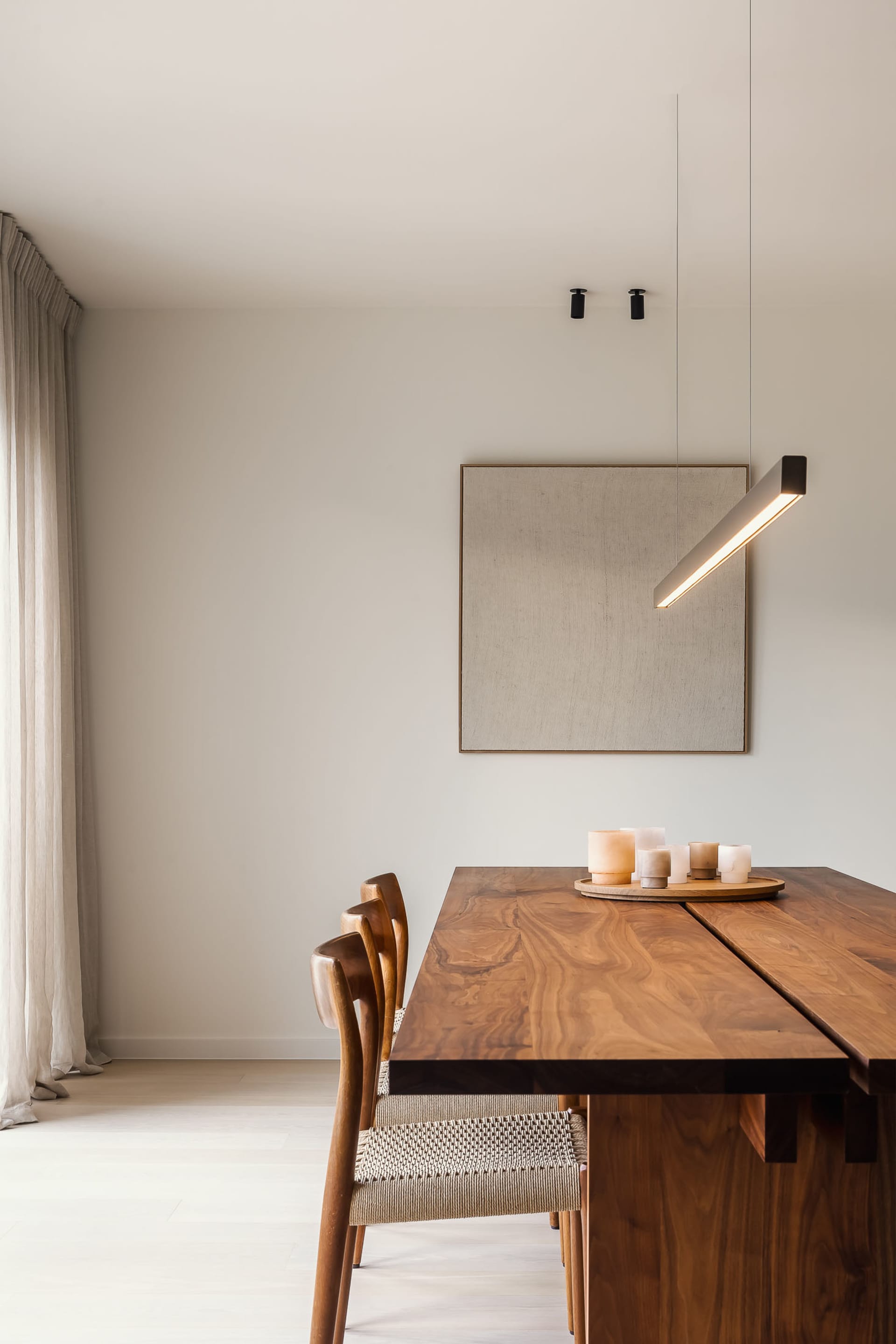 A minimalist dining room featuring a wooden table with a hanging lamp and candles.