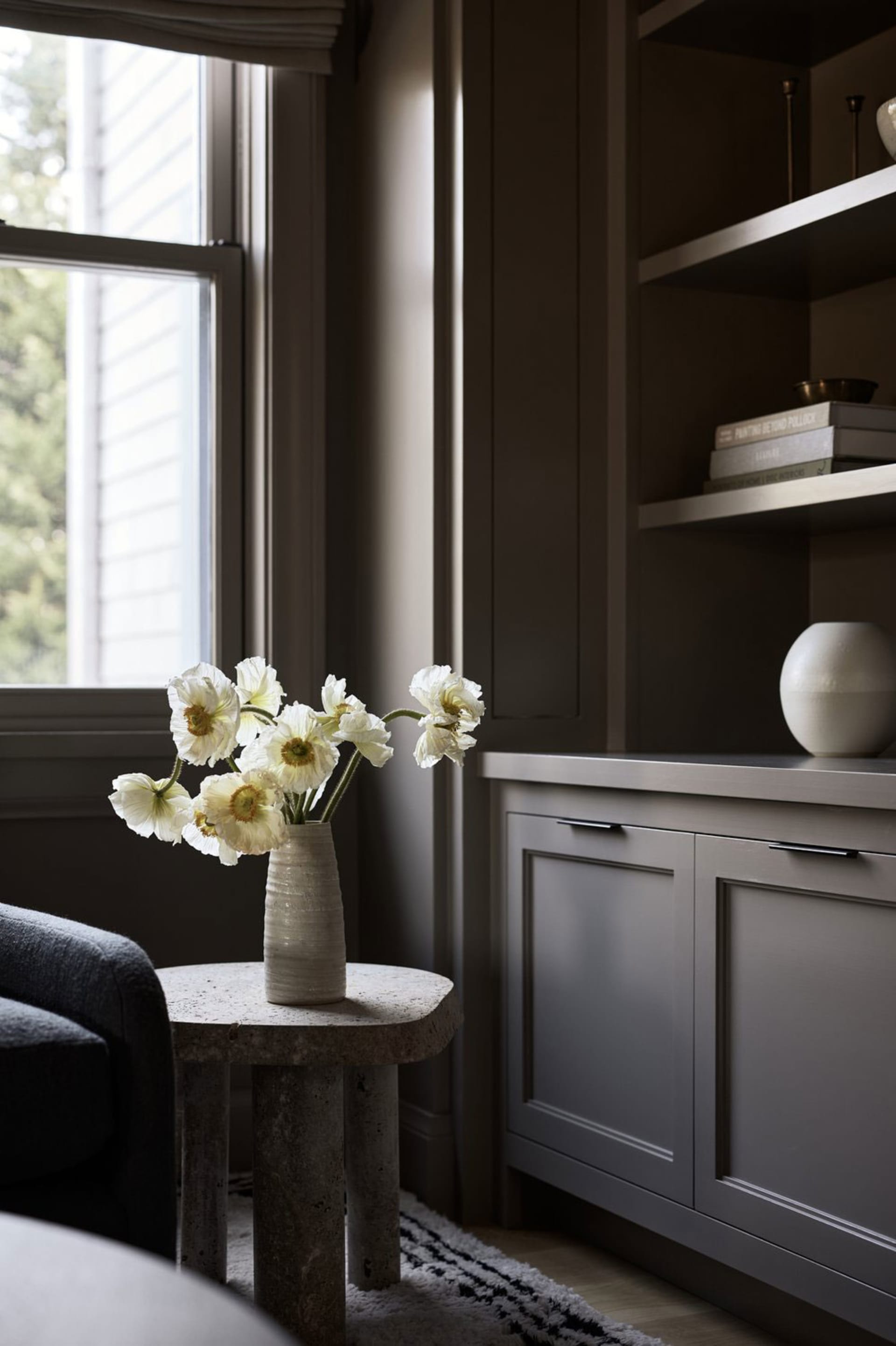 A modern living room with a grey concrete cabinet featuring white flowers in a vase.