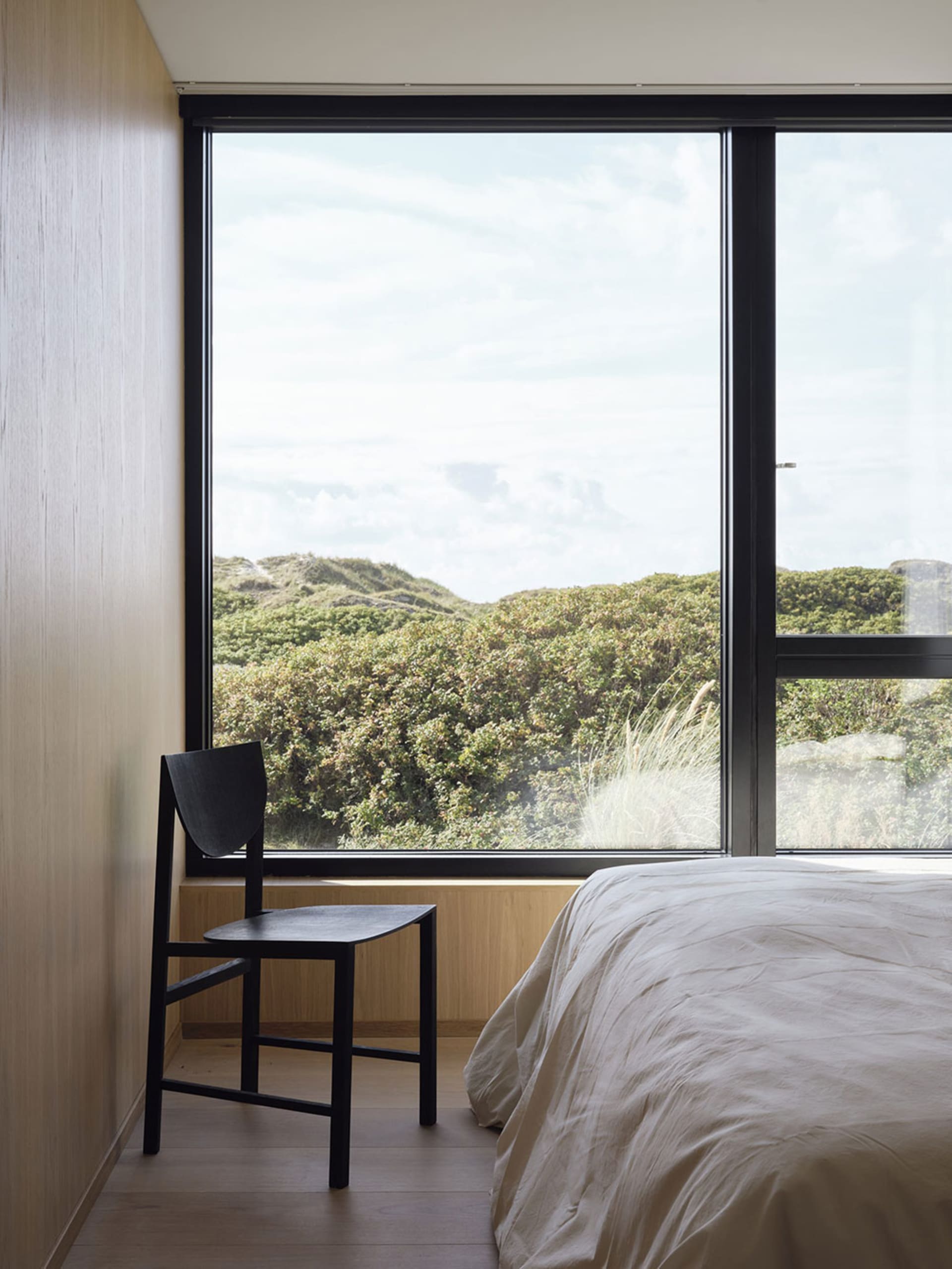 A minimalist bedroom with a large window overlooking greenery.