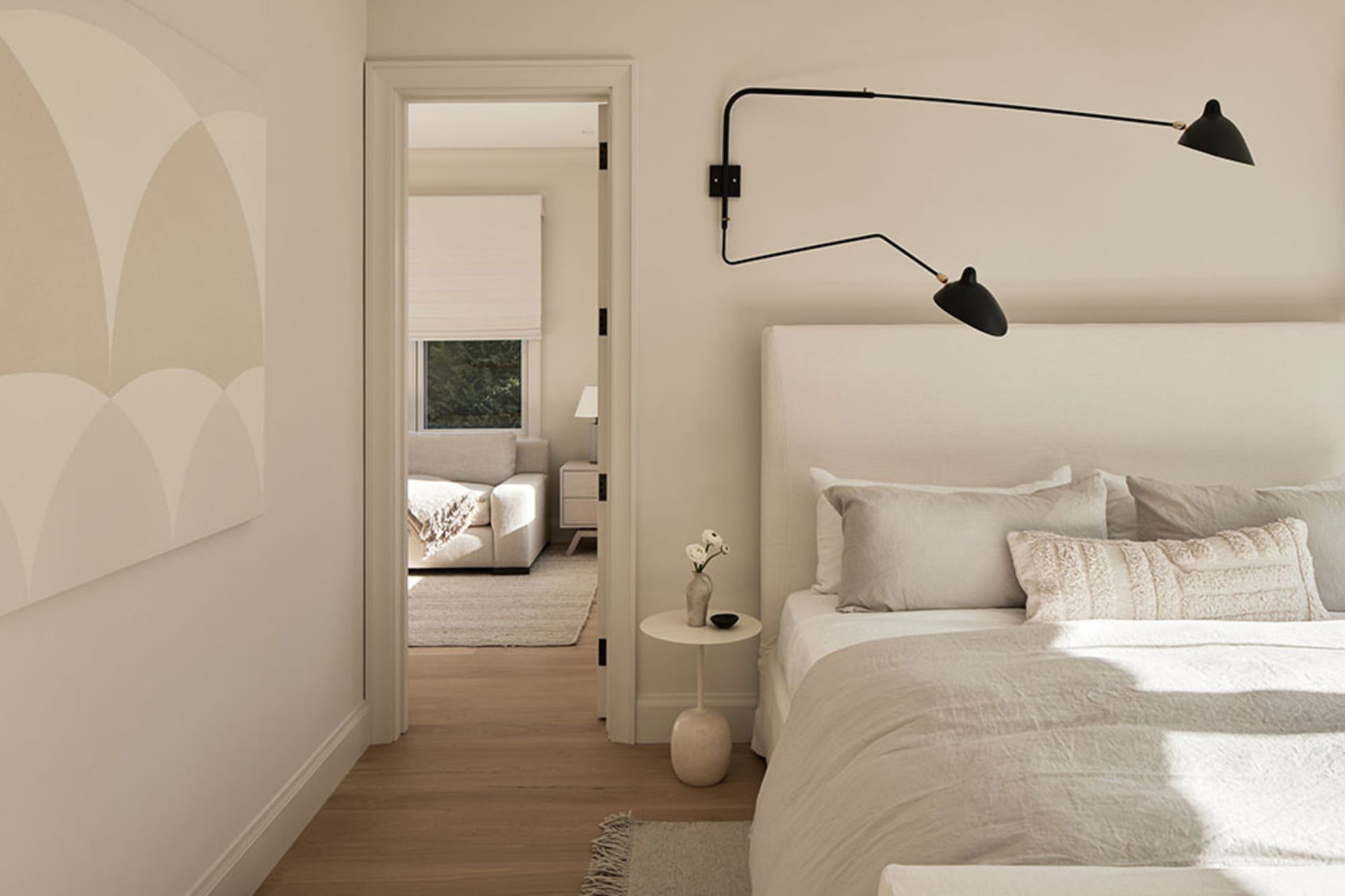 A modern minimalist bedroom with a simple white bed, white linens, and a soft fabric headboard.