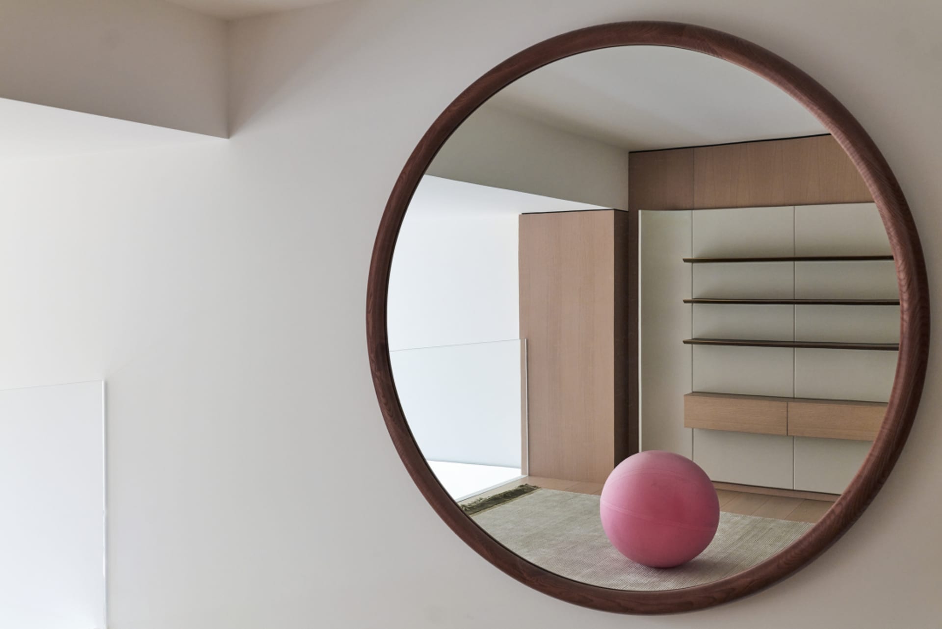 A minimalist room featuring wooden furniture and a pink ball on a rug.