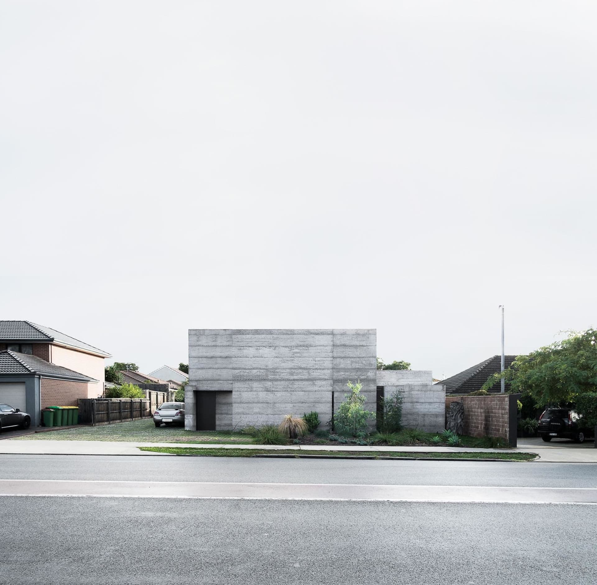 A modern concrete residential house with a minimalist aesthetic, featuring a single-story structure with a flat roof and mini
