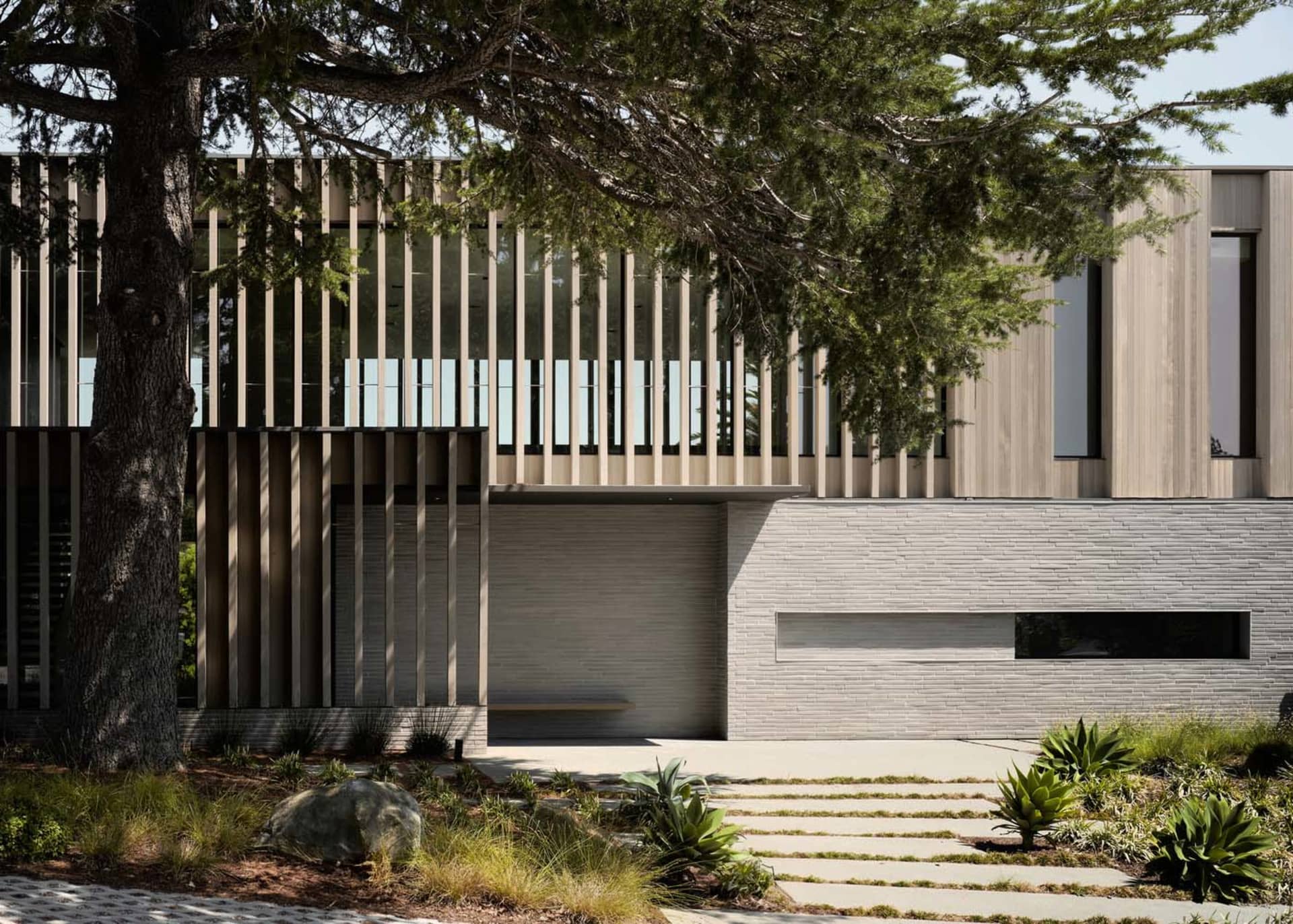 Modern exterior of a residential house featuring a wood cladding on the upper floor, with a minimalist driveway and landscapi