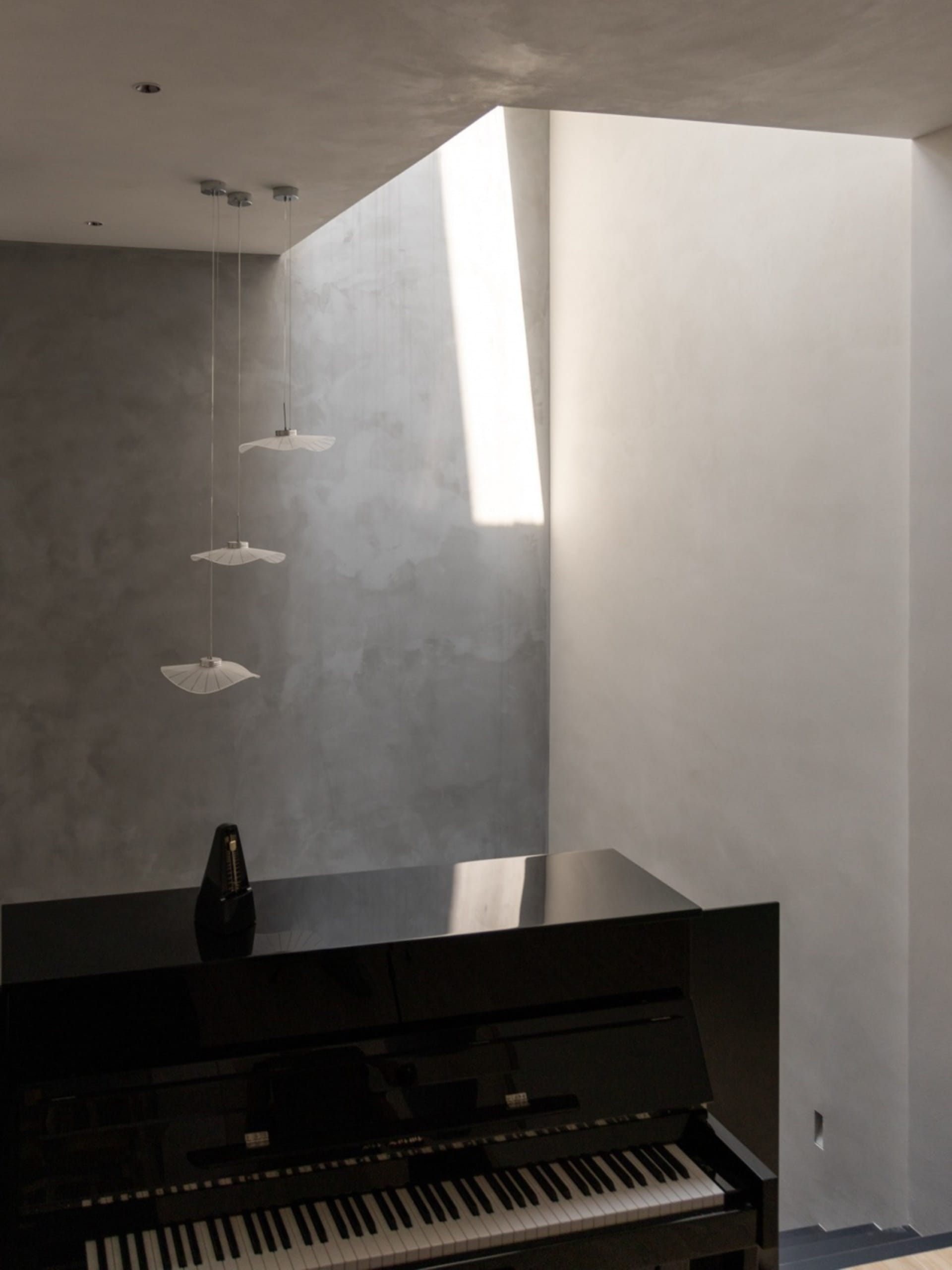 Modern minimalist music room with concrete walls, a piano, and pendant lights.