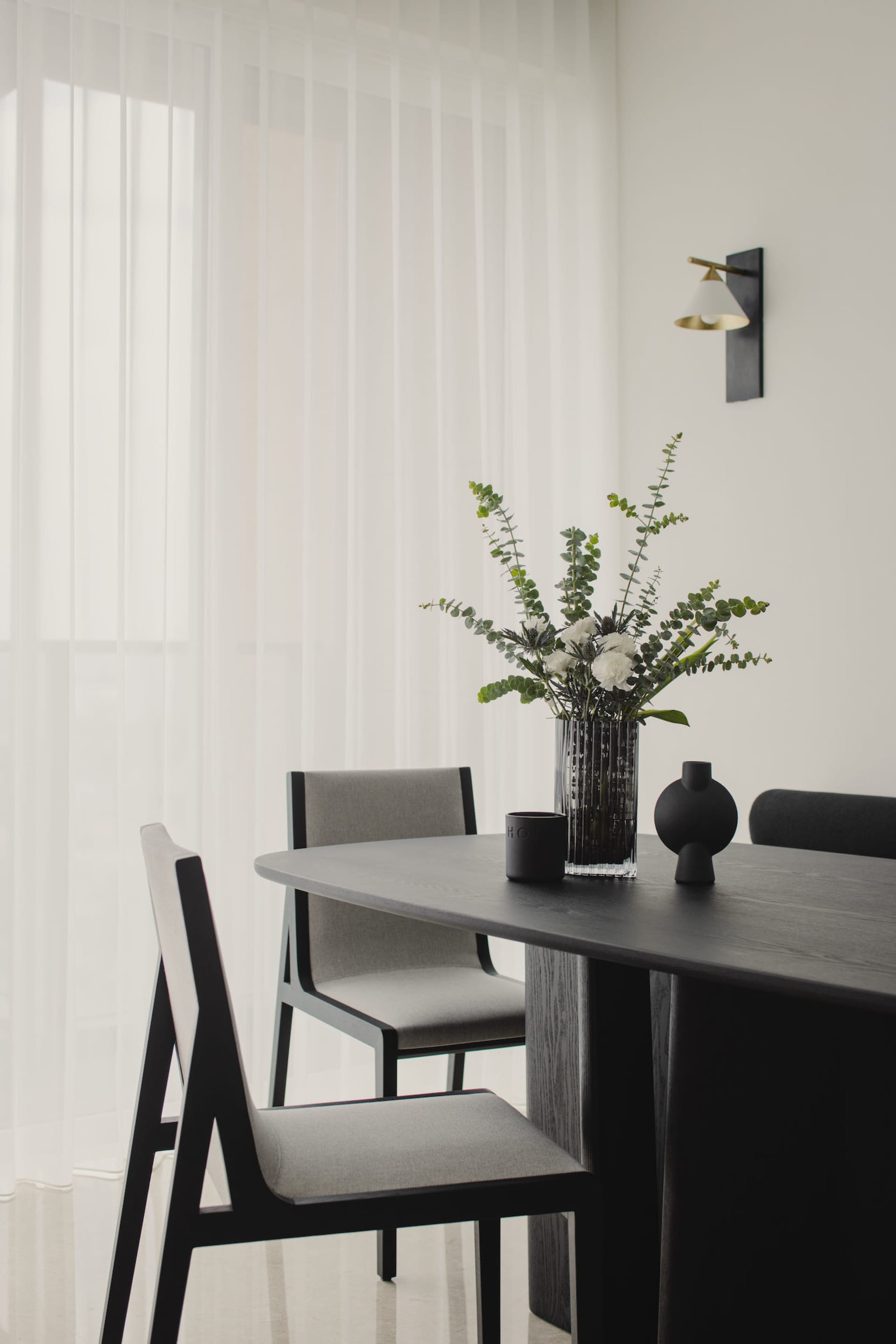 A modern dining room with wooden furniture, including chairs and a table, adorned with a vase of flowers and decorative objec