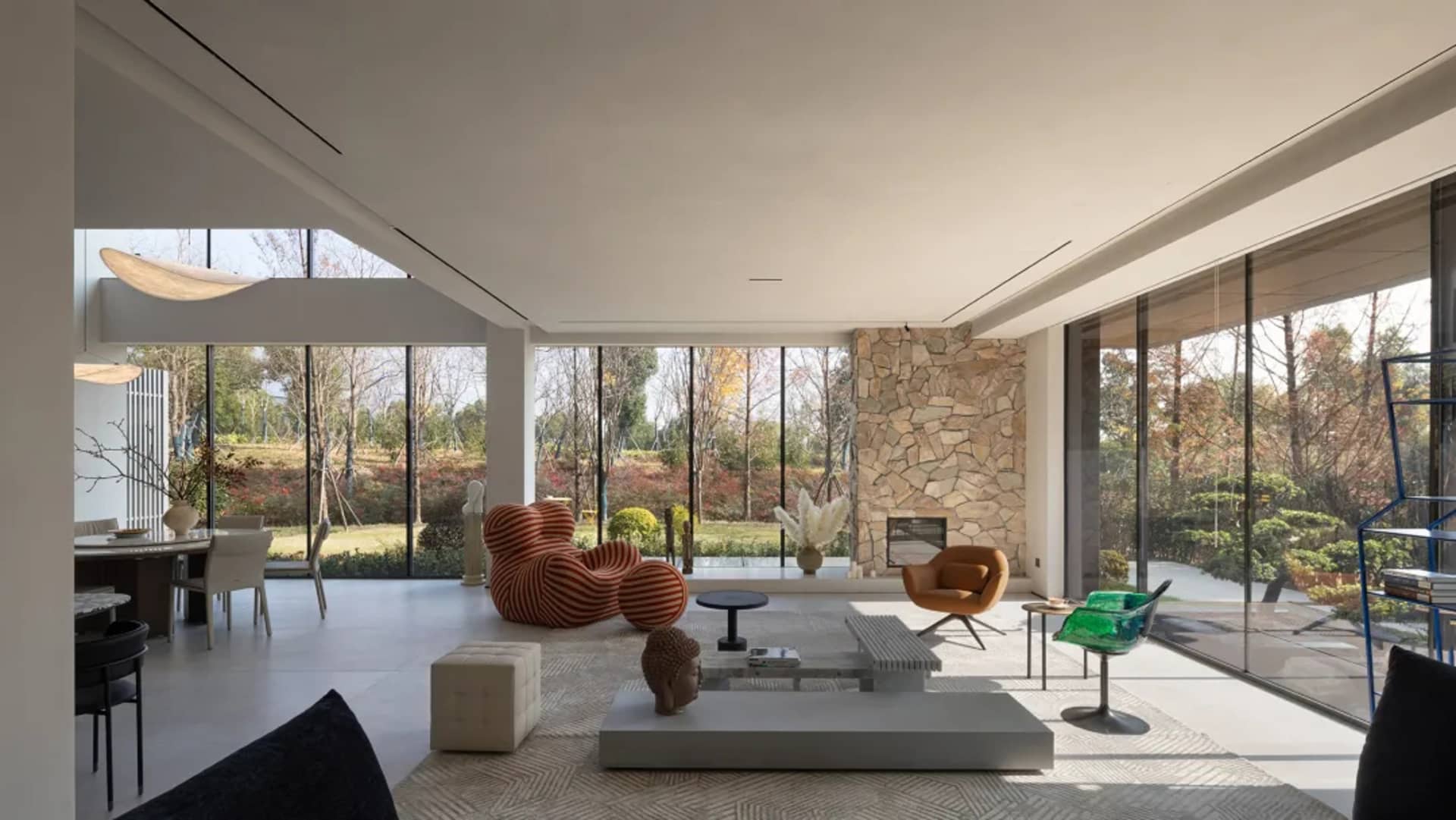 Modern living room with glass walls, featuring minimalist furniture and a stone fireplace.