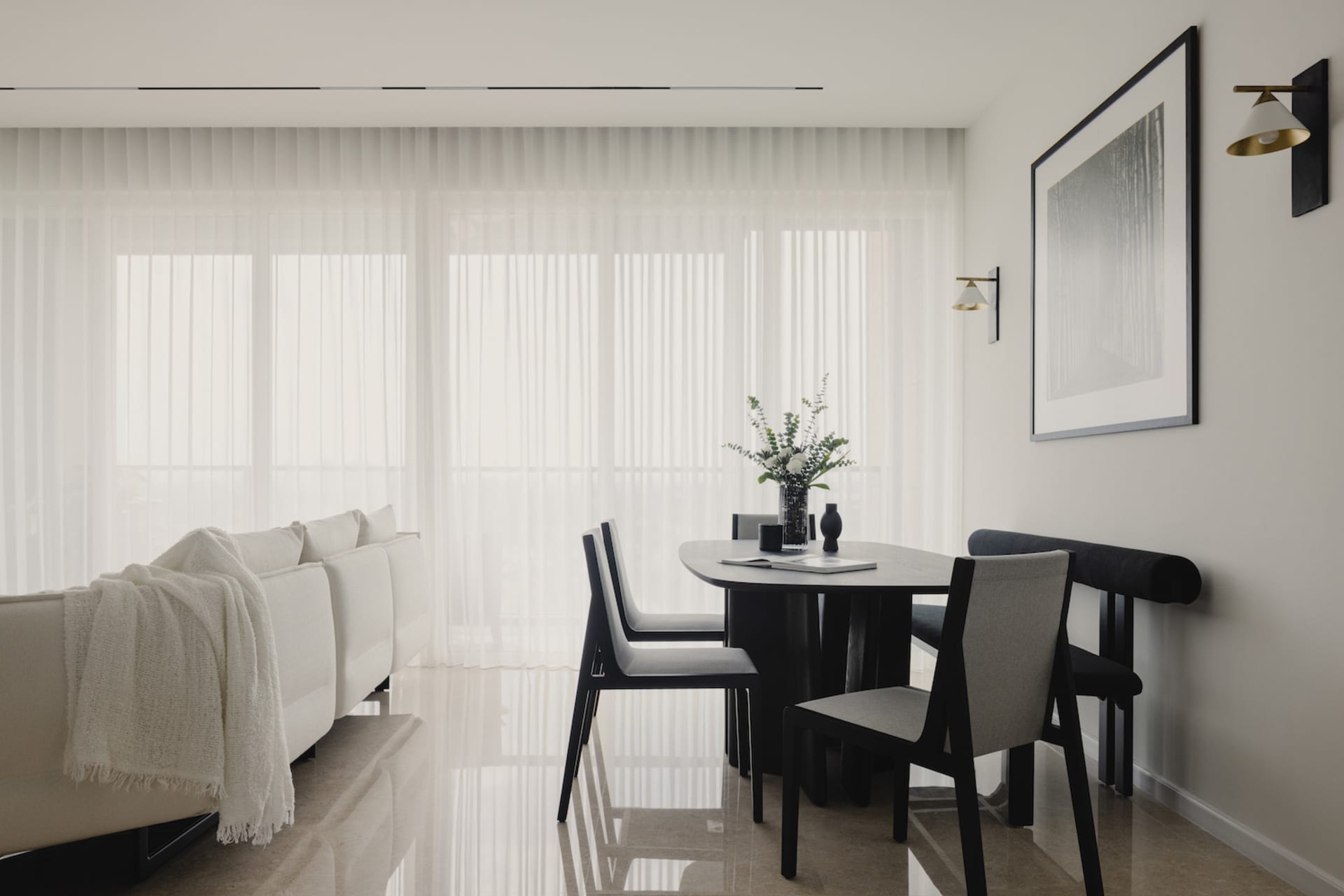 Modern minimalist dining room featuring neutral-toned furniture and a large window with sheer curtains, overlooking an indoor