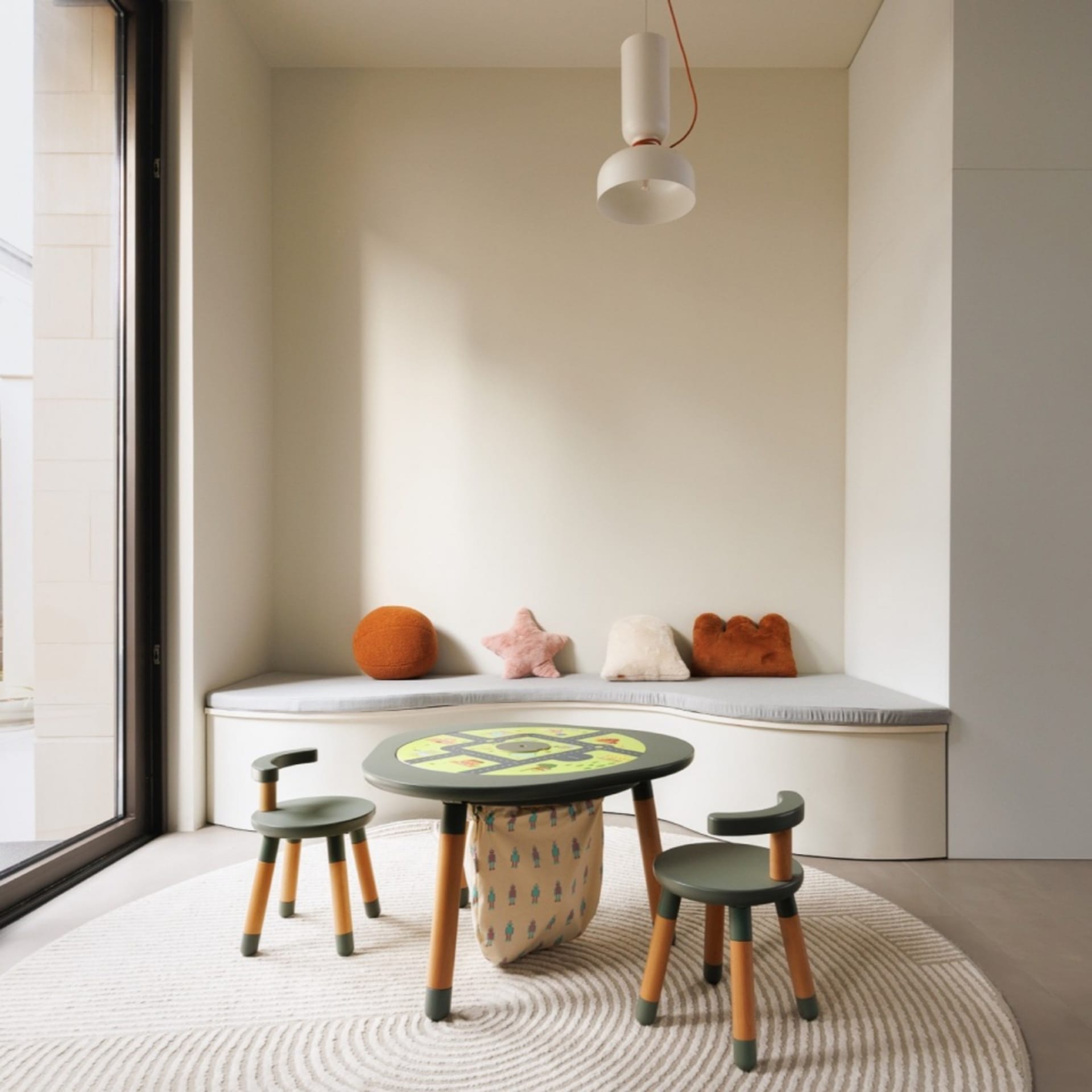Modern playroom with wooden furniture, including a table and chairs, and a cushioned bench with colorful pillows.