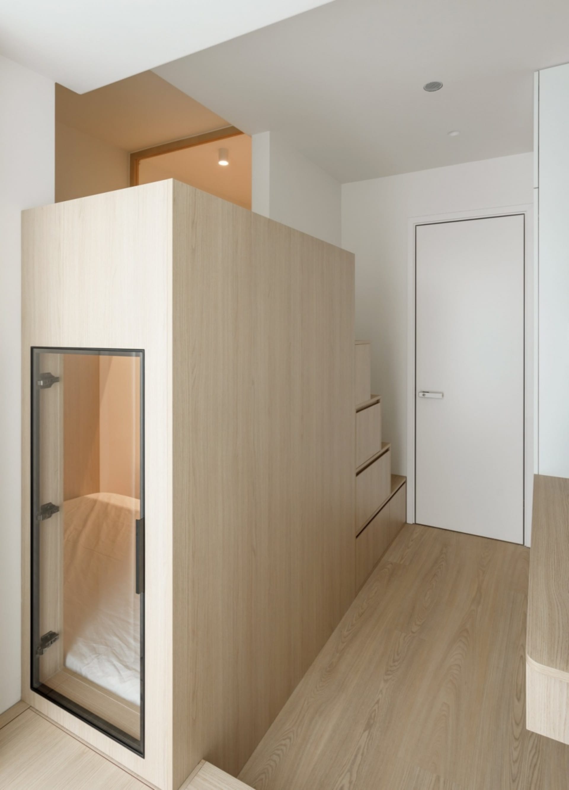 A minimalist interior design featuring a white door, wooden walls, and a glass panel.