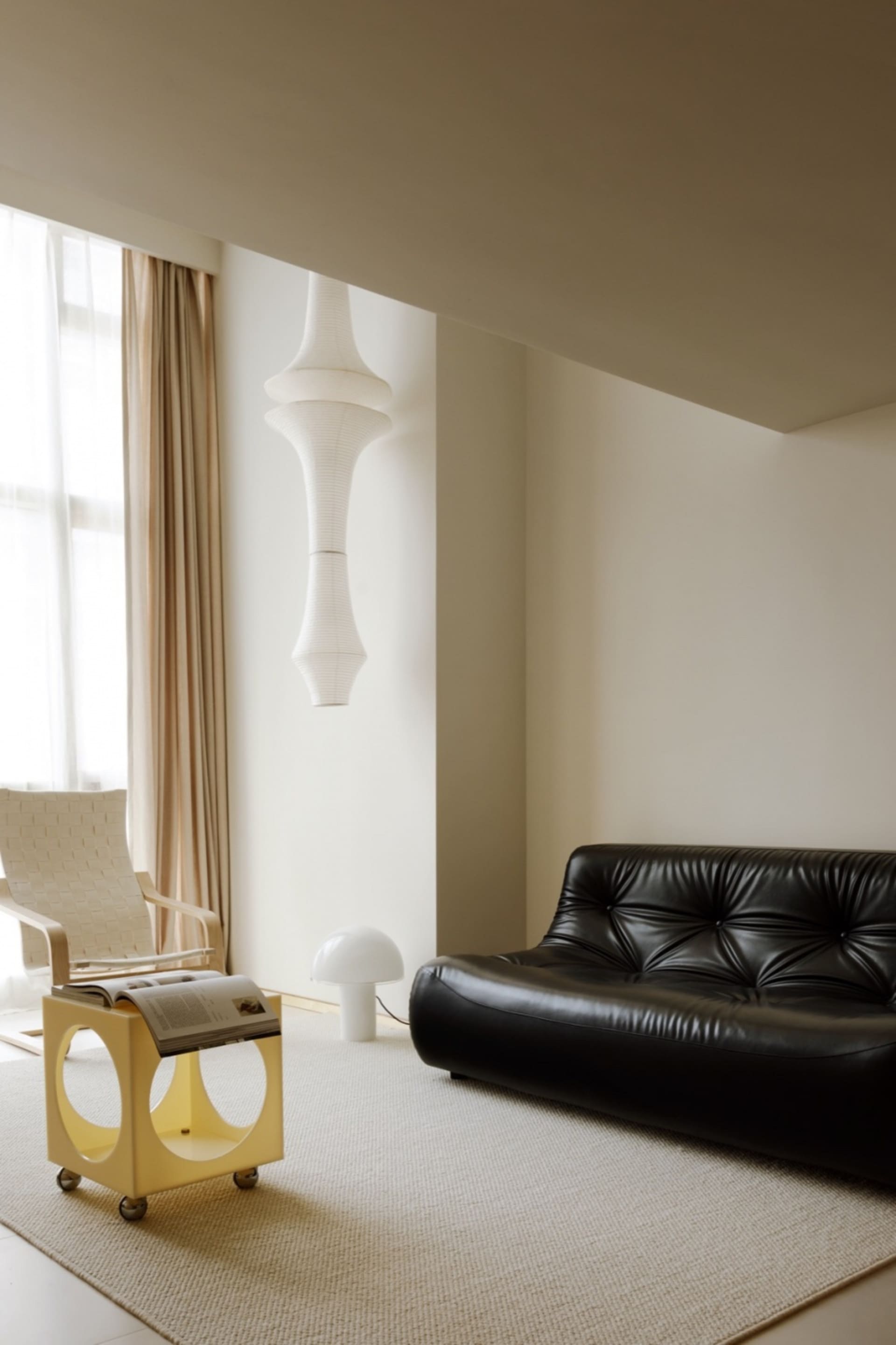 A minimalist living room features a sleek, black leather sofa and a vibrant yellow end table with wheels, set against a backg